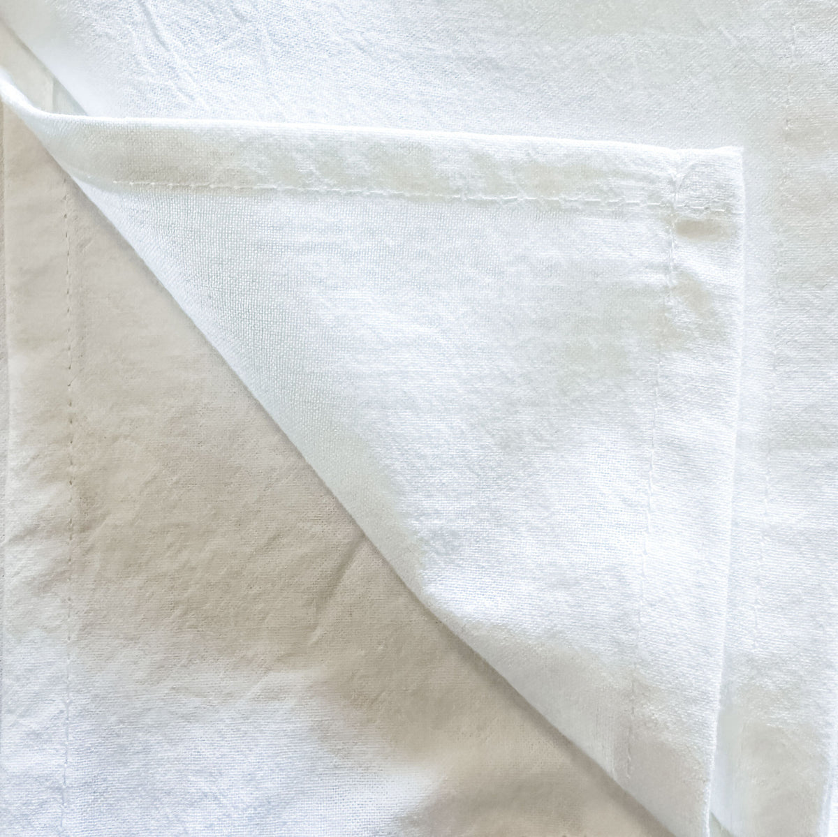 Close-up of the folded corner of a white cotton tea towel, showing the hemmed edge.