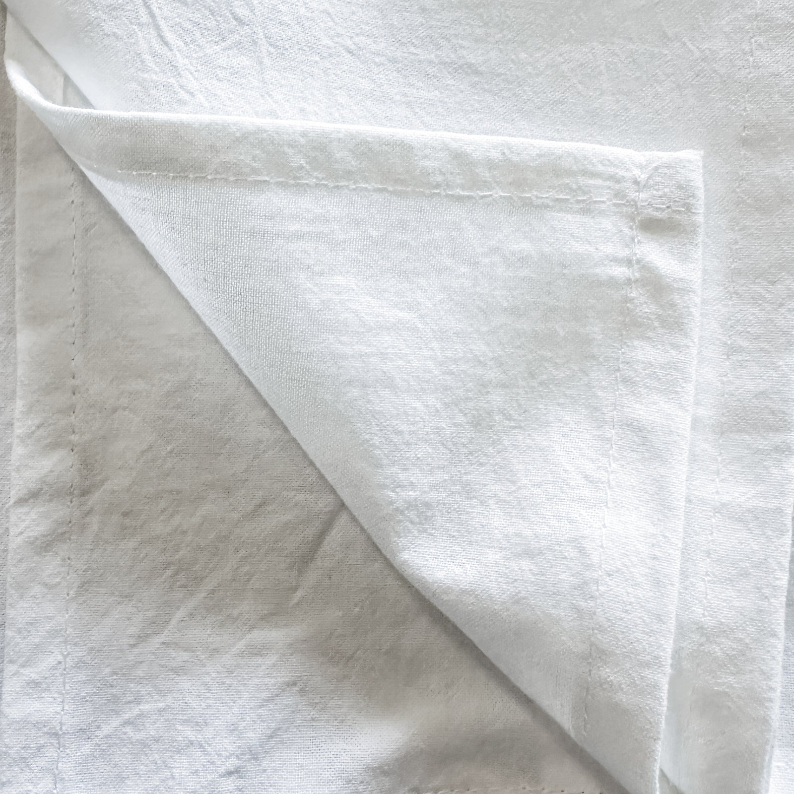 Close-up of the folded corner of a white cotton tea towel, showing the hemmed edge.