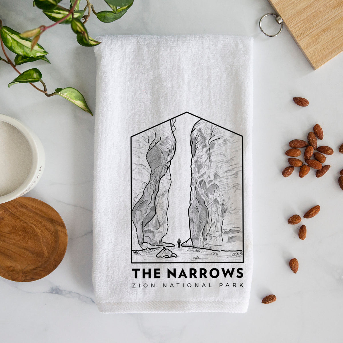 White hand towel printed with a black line art badge of the tall canyon walls of The Narrows, with the words The Narrows.