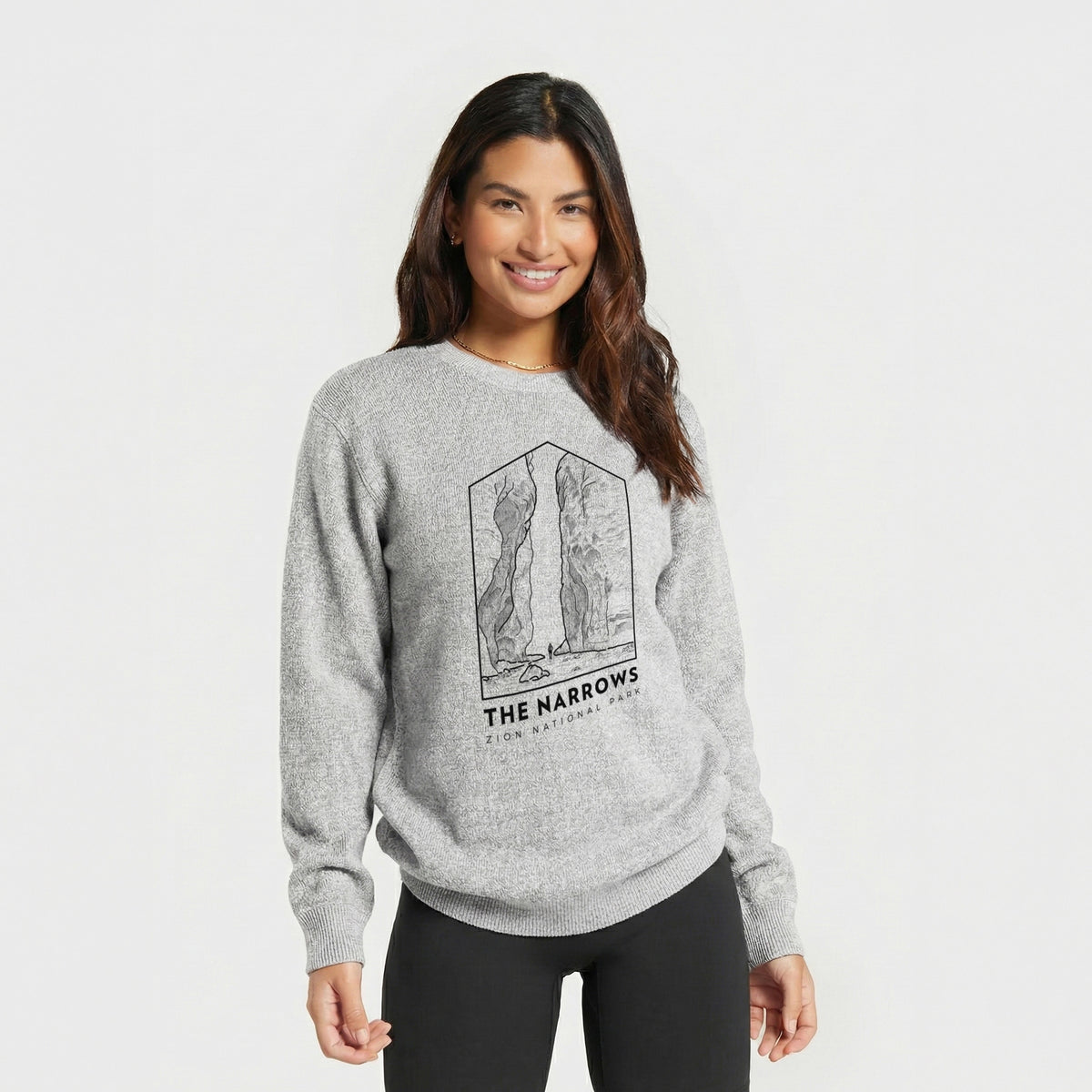 Woman wearing a knit sweatshirt printed with a black line art badge of the tall canyon walls of The Narrows, with the words The Narrows.