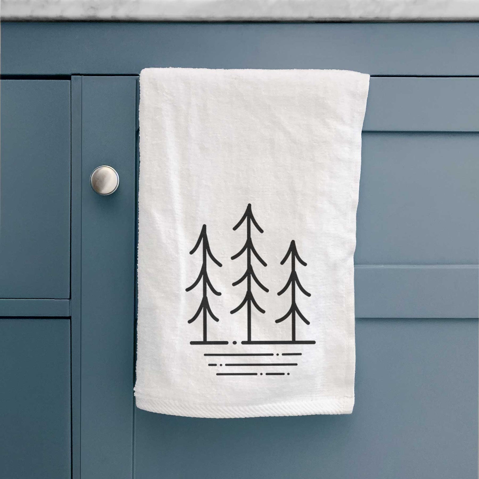 White hand towel printed with black line art of three simple pine trees above horizontal lines.