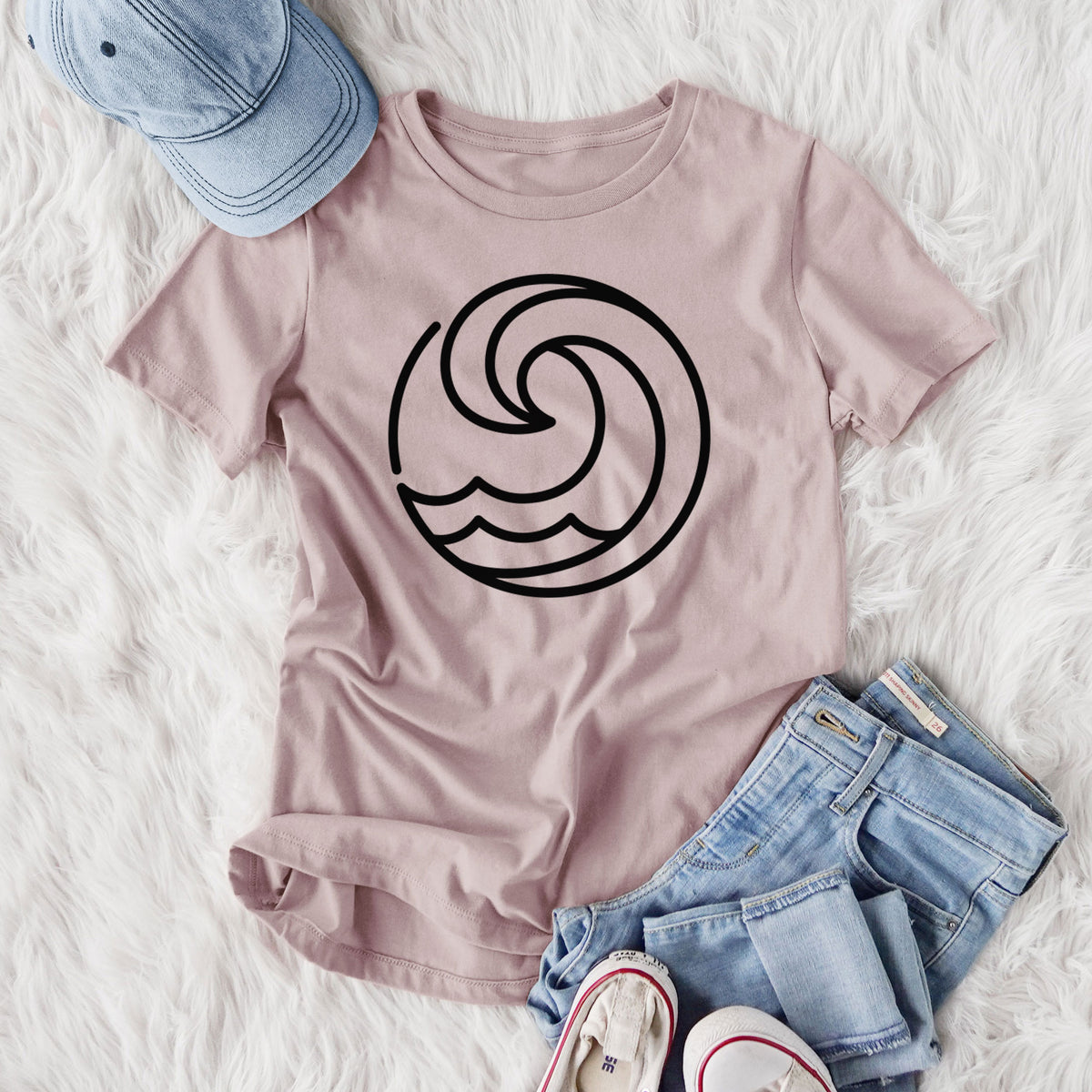 Women's relaxed fit cotton t-shirt printed with a bold black line art circle of a curling ocean wave, styled flat on a white faux fur rug with jeans.
