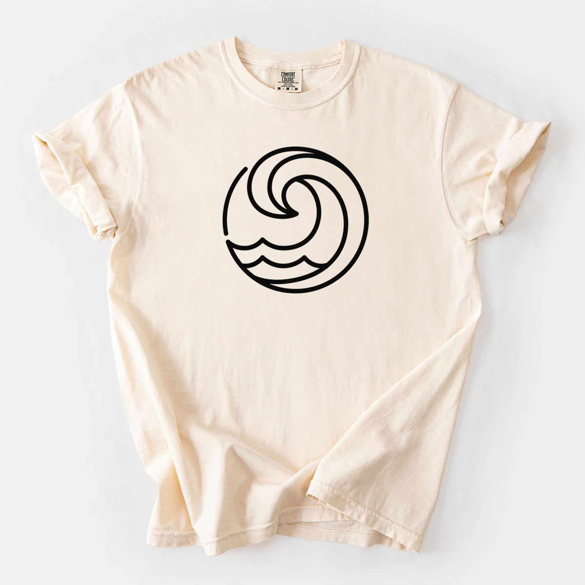 Ivory Comfort Colors t-shirt laid flat, printed with a bold black line art circle of a curling ocean wave.
