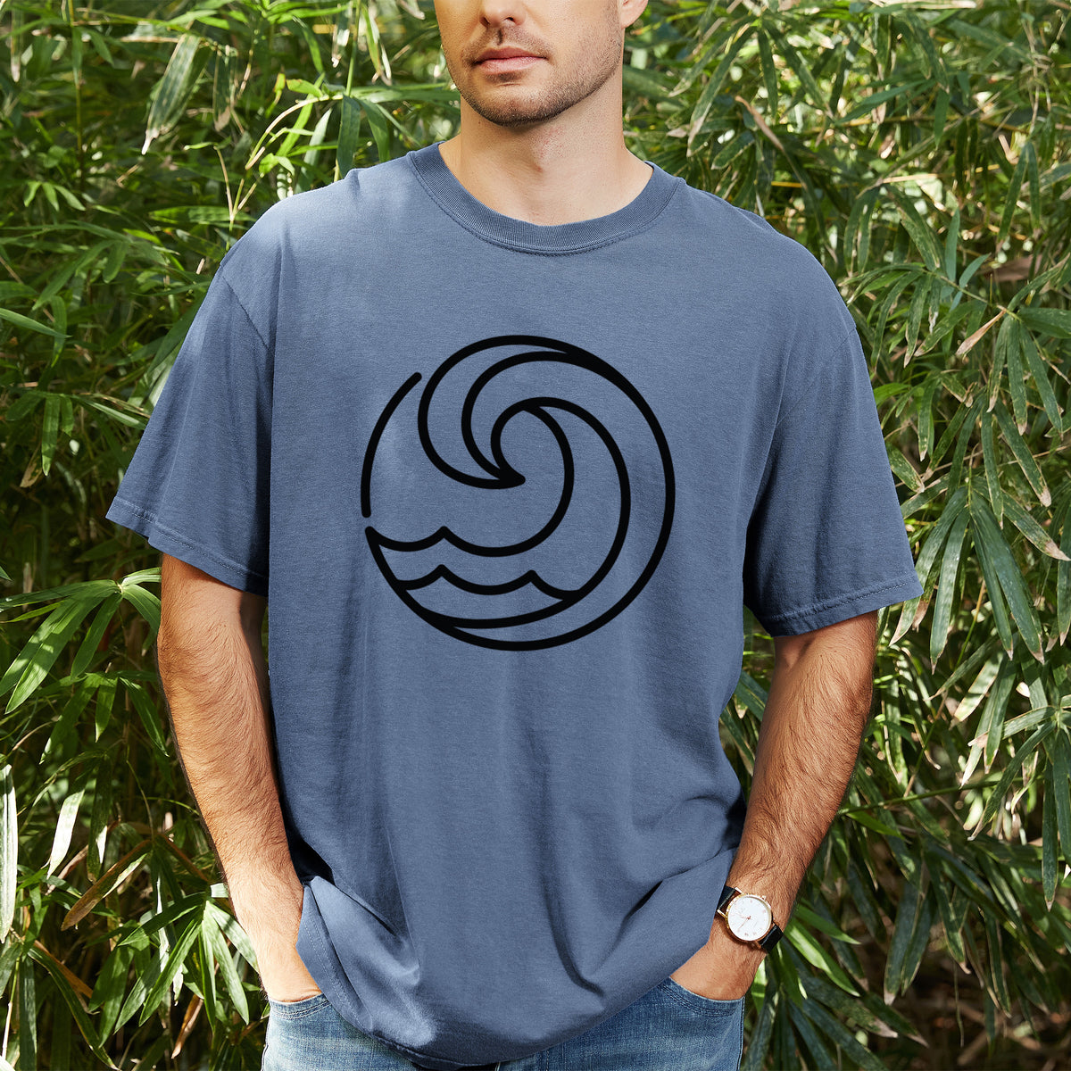 Man wearing a Comfort Colors t-shirt printed with a bold black line art circle of a curling ocean wave, outdoors.