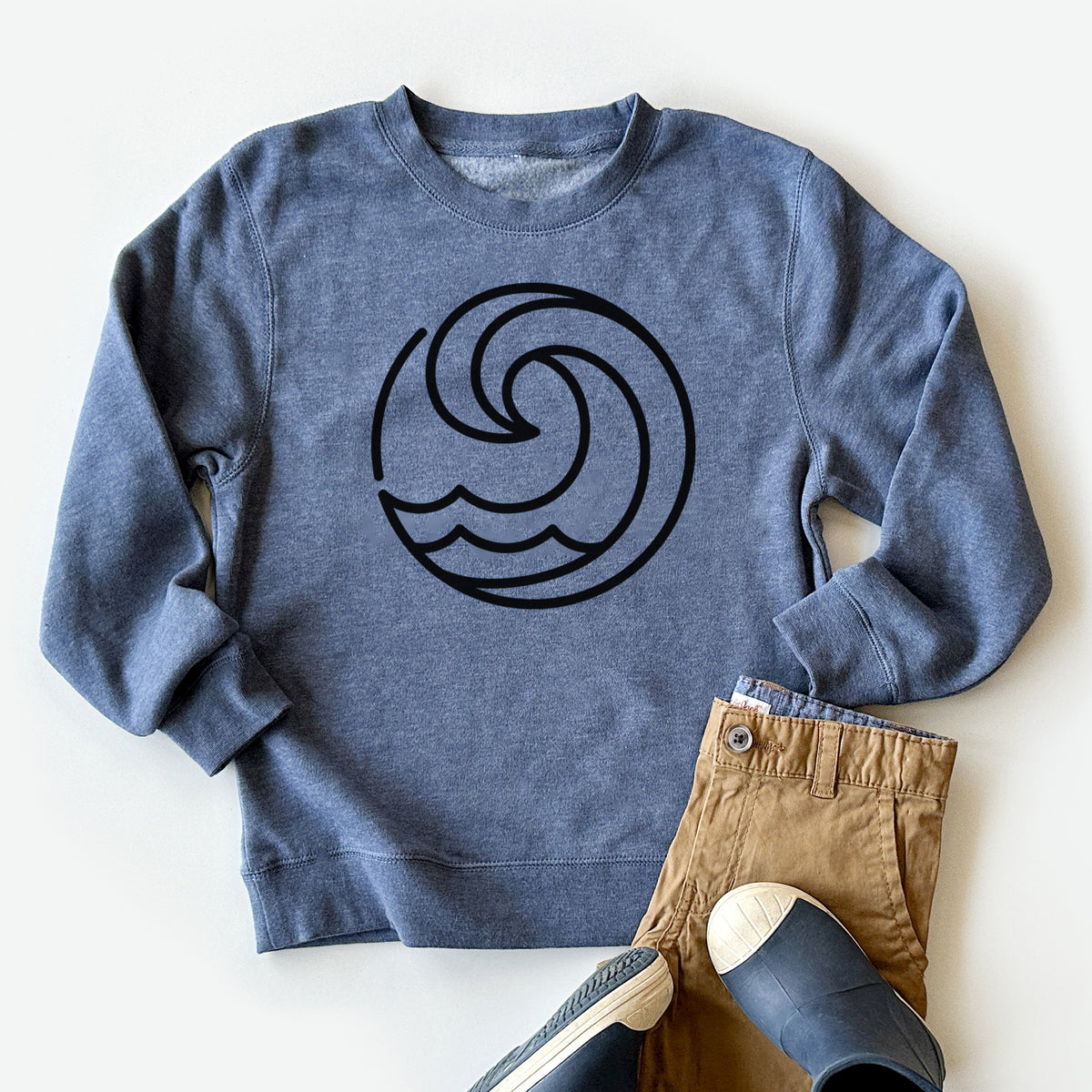 Youth crewneck sweatshirt printed with a bold black line art circle of a curling ocean wave, styled flat with khaki pants and shoes.
