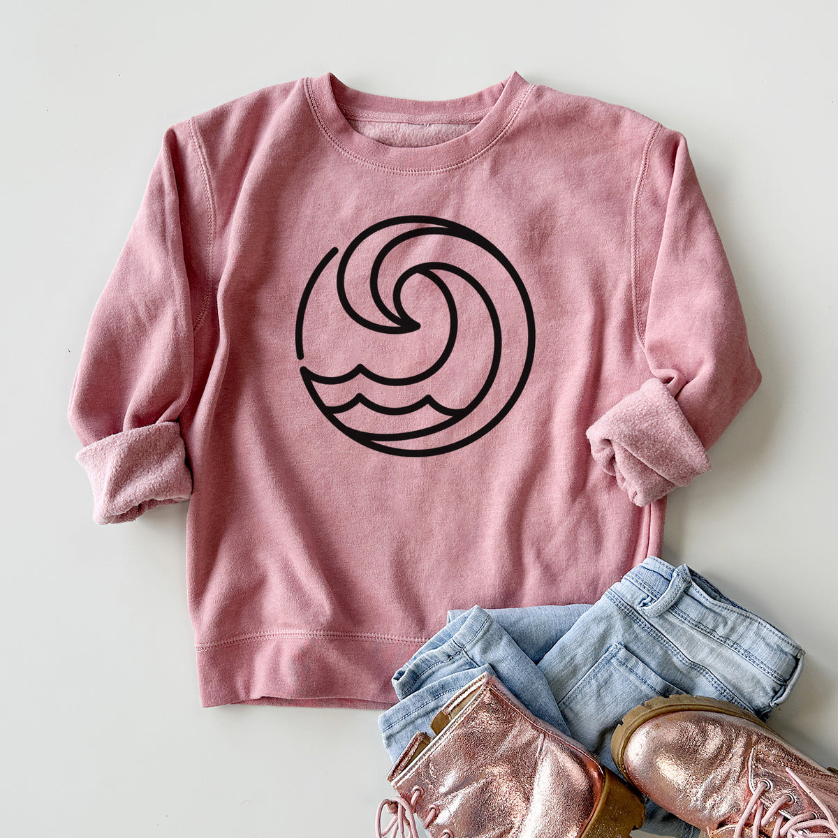 Youth crewneck sweatshirt printed with a bold black line art circle of a curling ocean wave, styled flat with jeans and boots.