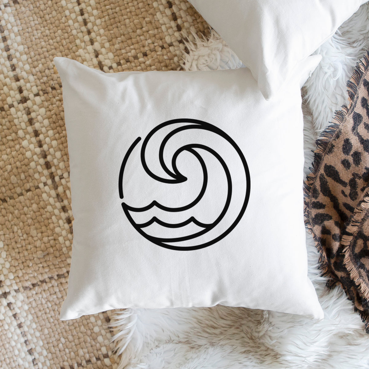 White pillow cover printed with a bold black line art circle of a curling ocean wave, on a woven chair.