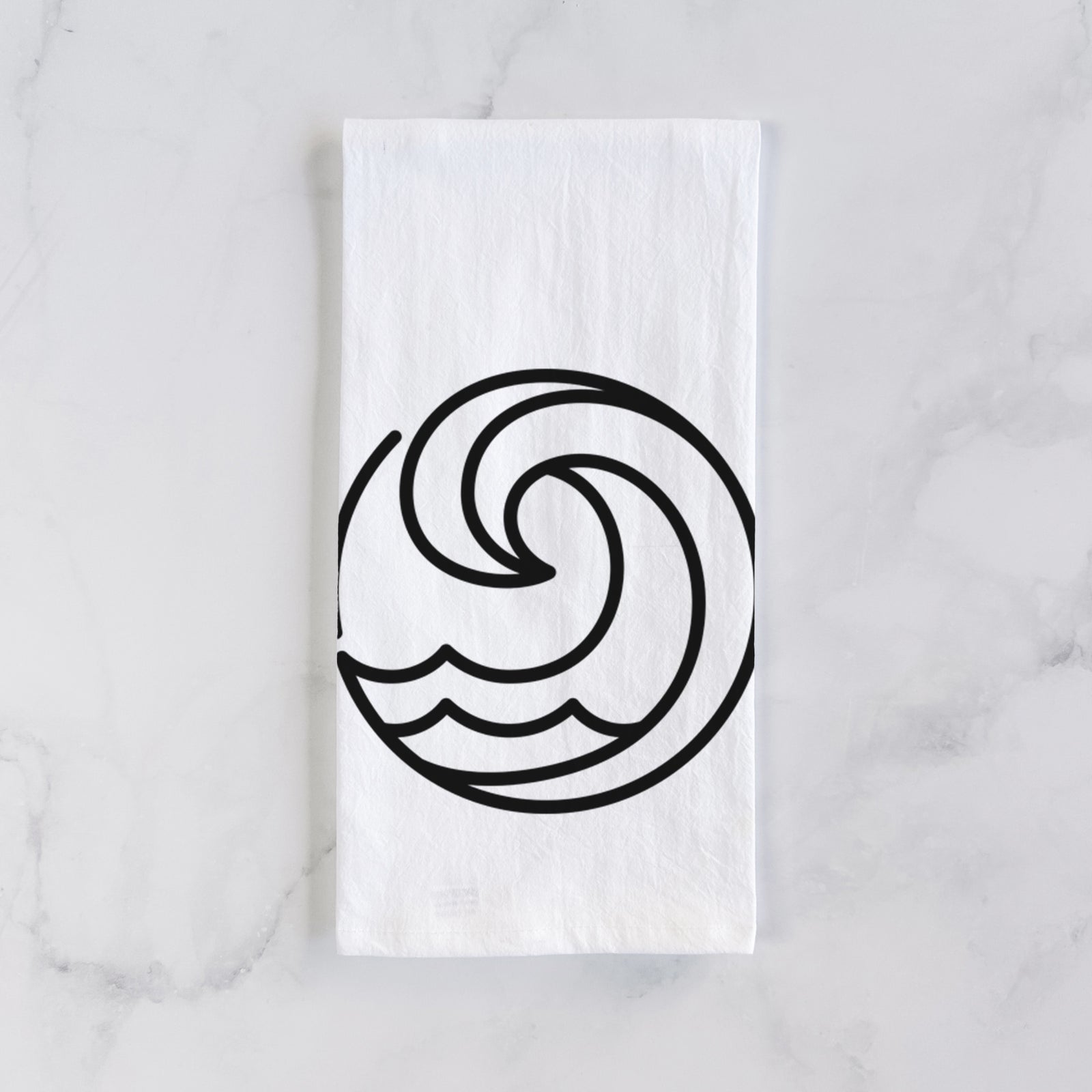 White cotton tea towel printed with a bold black line art circle of a curling ocean wave, on a marble counter beside a round wooden cutting board and greenery.