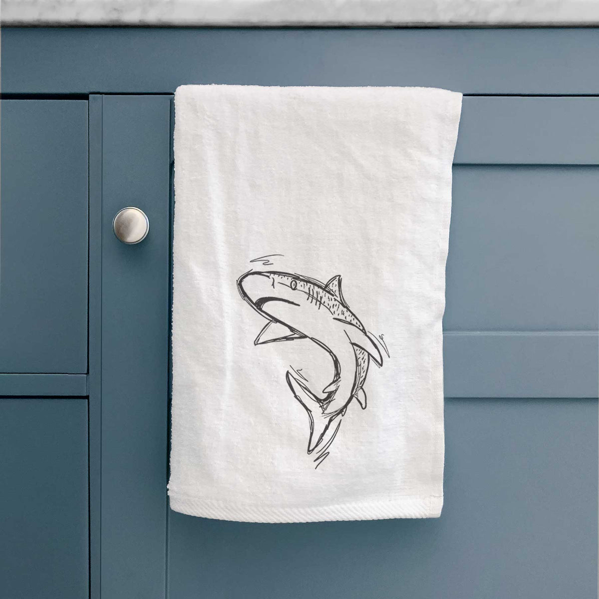 White hand towel printed with a black ink illustration of a tiger shark swimming in a curve, hanging on a cabinet door.