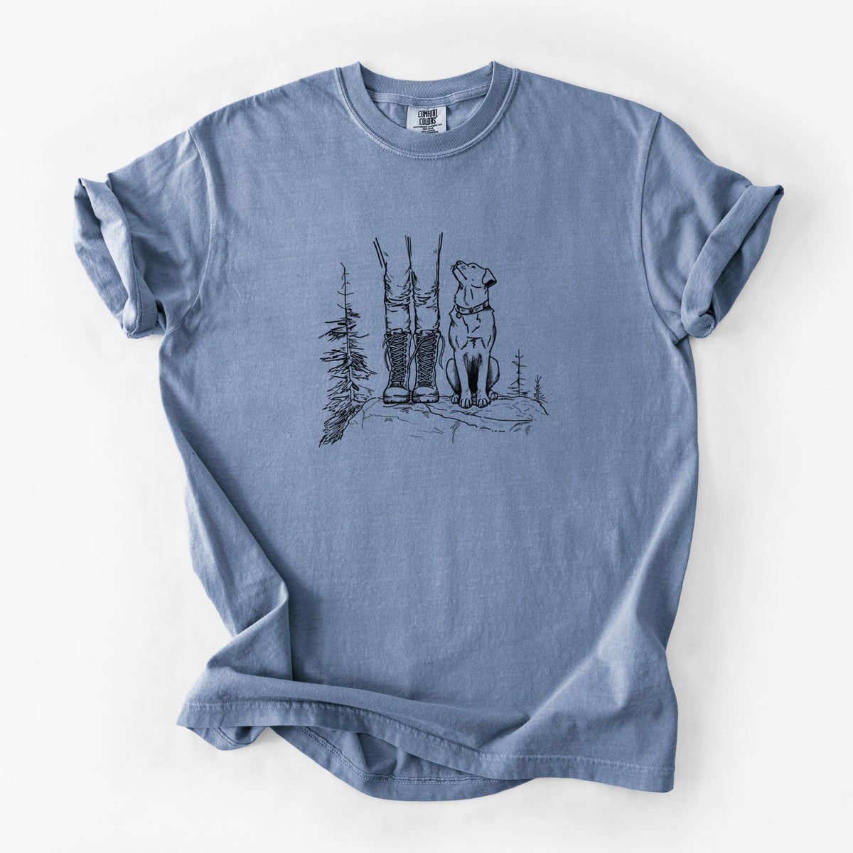 Blue jean Comfort Colors t-shirt laid flat, printed with a black ink illustration of a hiker in boots and a dog sitting side by side on a forest trail, seen from behind.