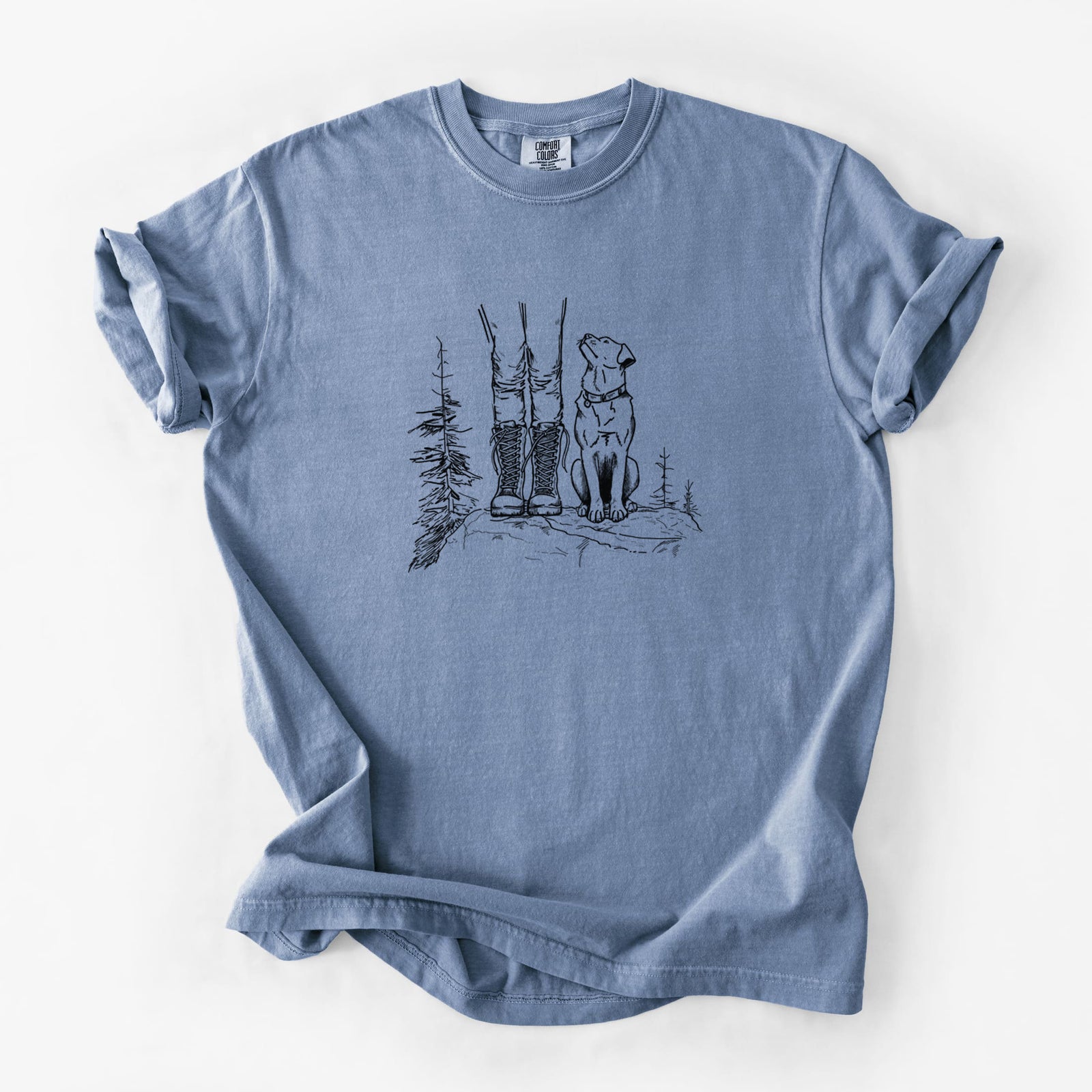 Blue jean Comfort Colors t-shirt laid flat, printed with a black ink illustration of a hiker in boots and a dog sitting side by side on a forest trail, seen from behind.