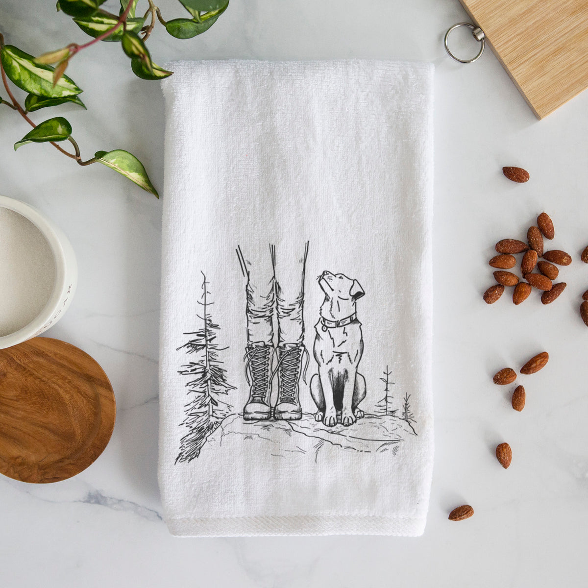 White hand towel printed with a black ink illustration of a hiker in boots and a dog sitting side by side on a forest trail, seen from behind.