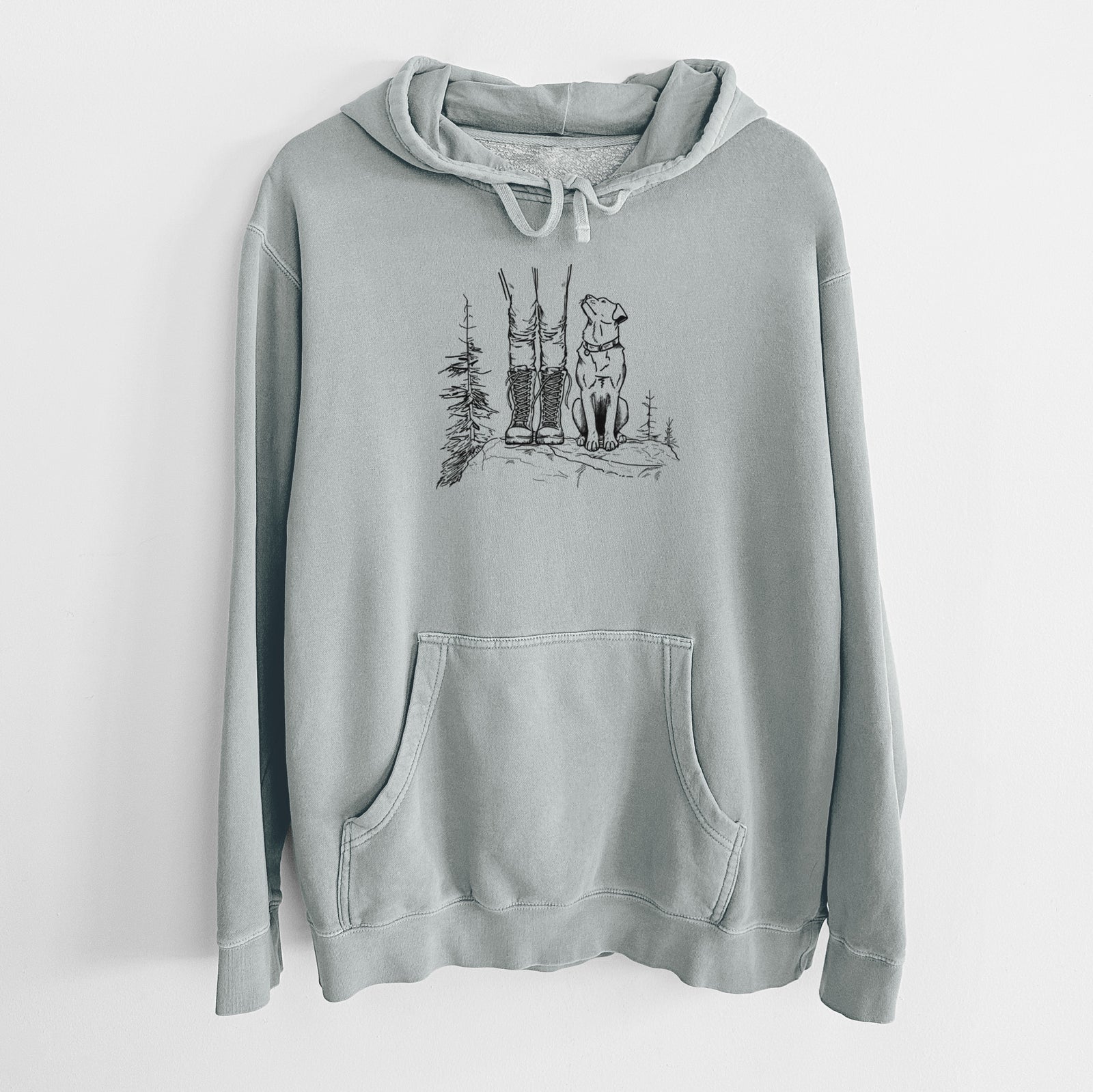 Sage green pigment dyed hoodie laid flat, printed with a black ink illustration of a hiker in boots and a dog sitting side by side on a forest trail, seen from behind.