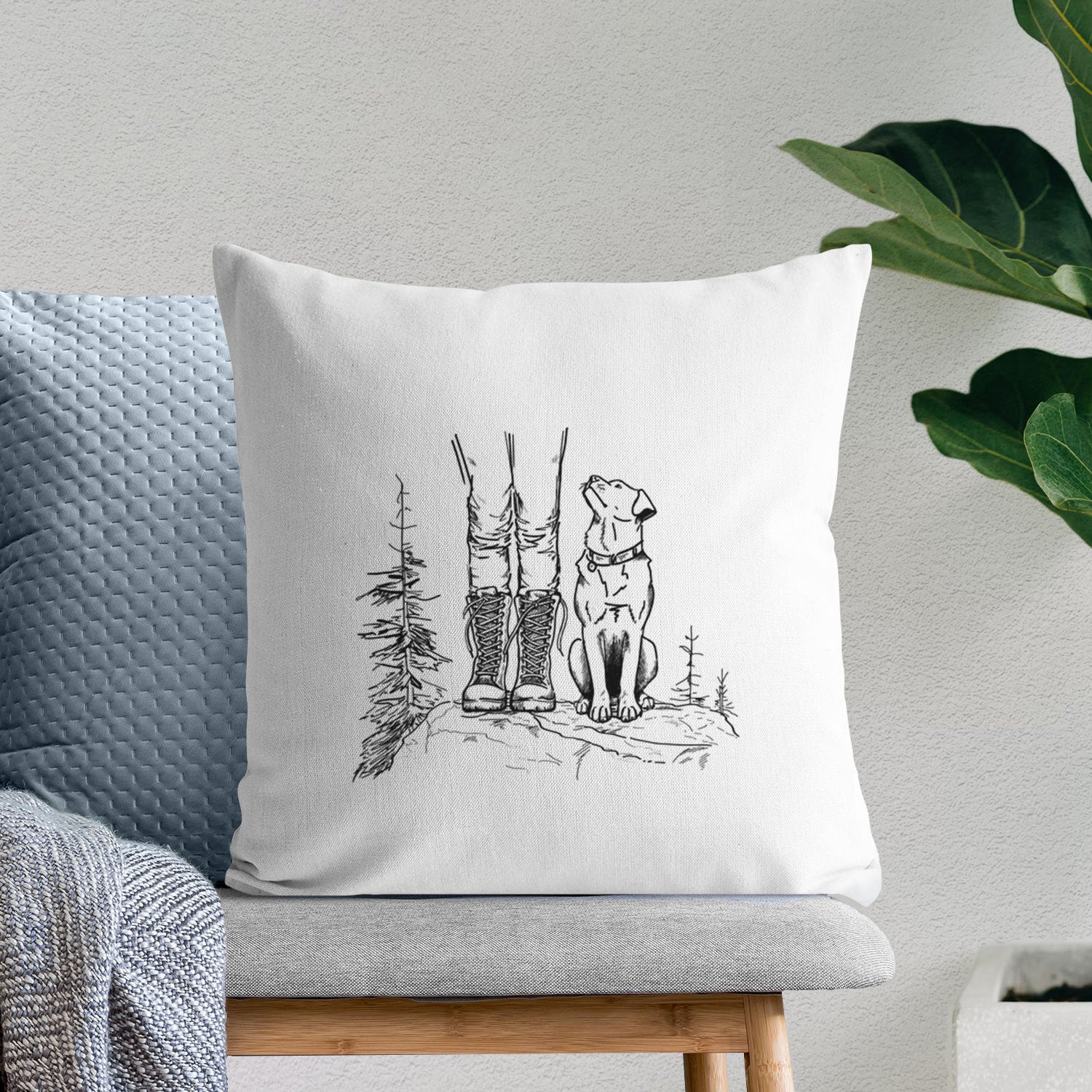 White pillow cover printed with a black ink illustration of a hiker in boots and a dog sitting side by side on a forest trail, seen from behind, on a bench beside plants.