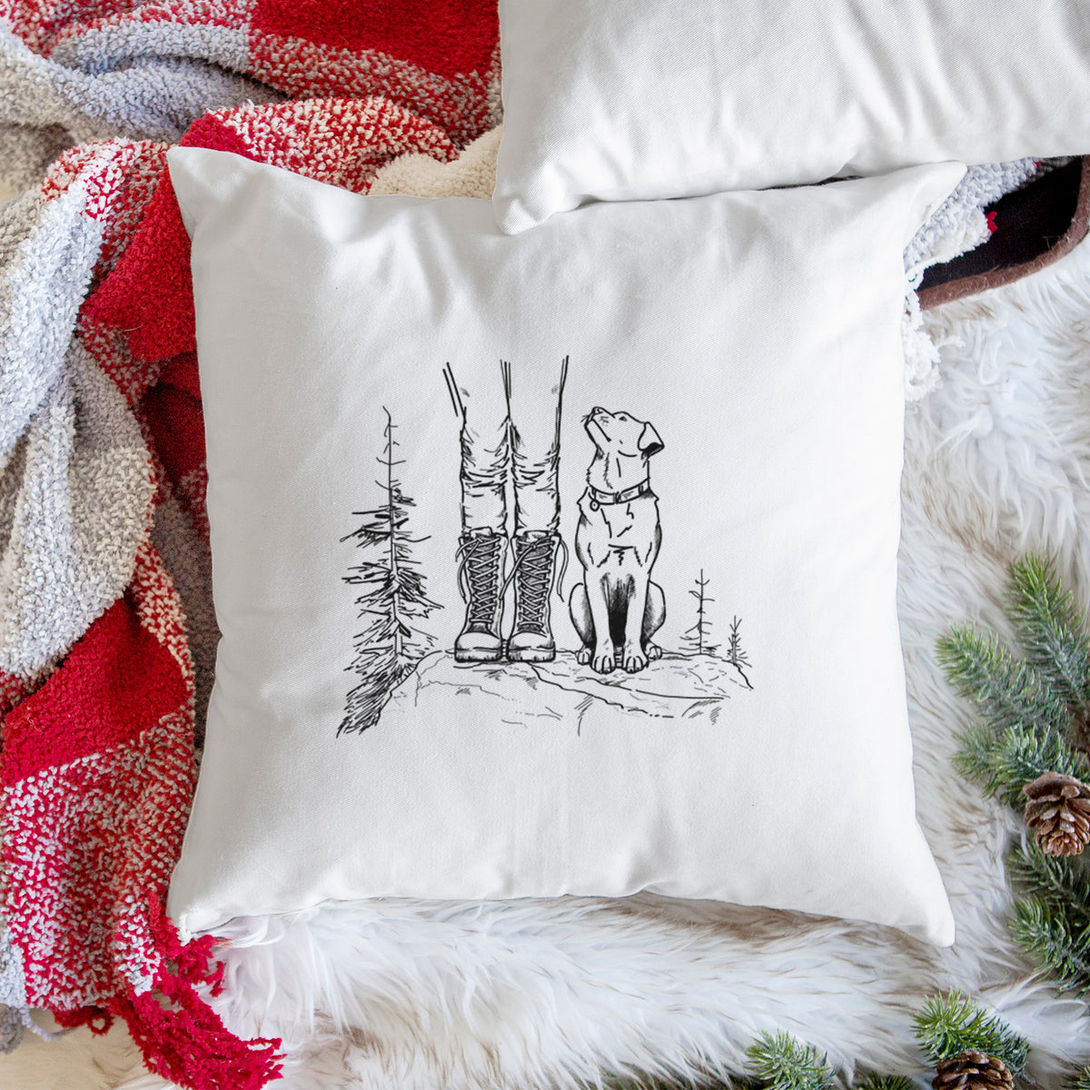 White pillow cover printed with a black ink illustration of a hiker in boots and a dog sitting side by side on a forest trail, seen from behind, on a woven chair.
