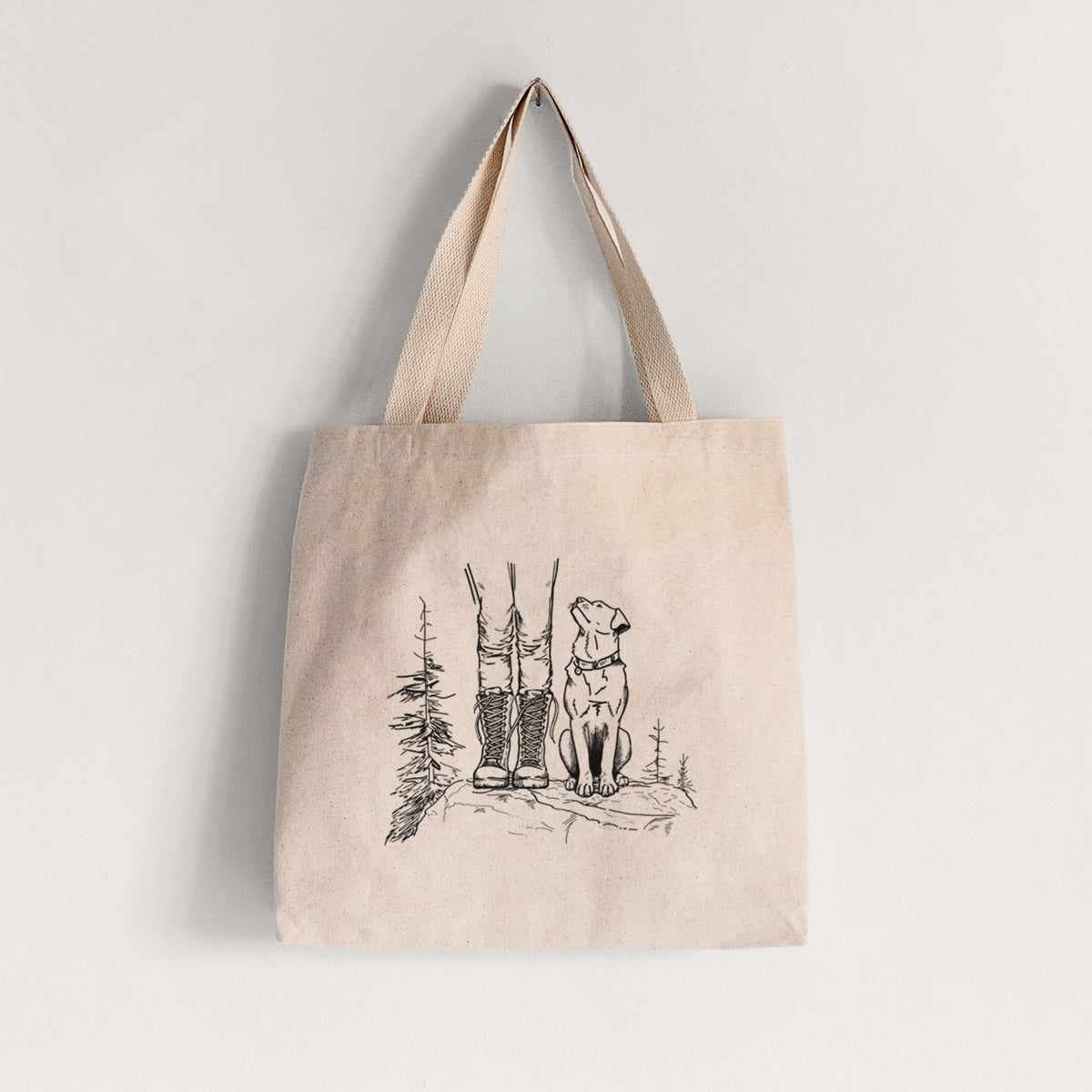 Natural canvas tote bag printed with a black ink illustration of a hiker in boots and a dog sitting side by side on a forest trail, seen from behind.
