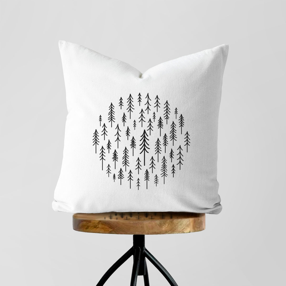 White pillow cover printed with a circle made of small black ink pine trees, on a wooden stool.