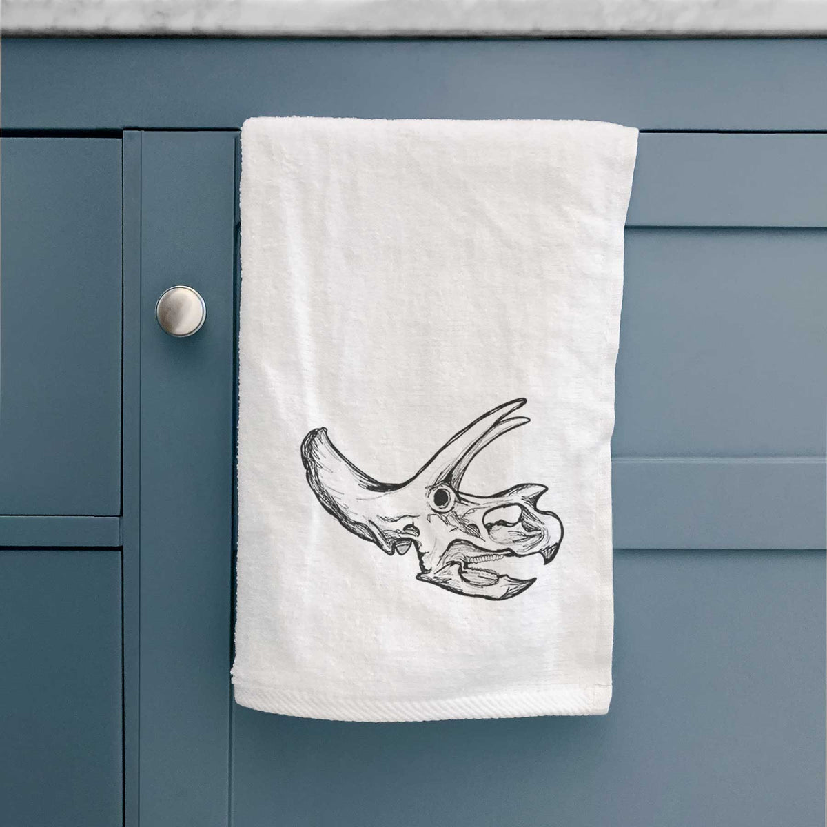 White hand towel printed with a detailed black ink illustration of a Triceratops skull with its horns and frill.