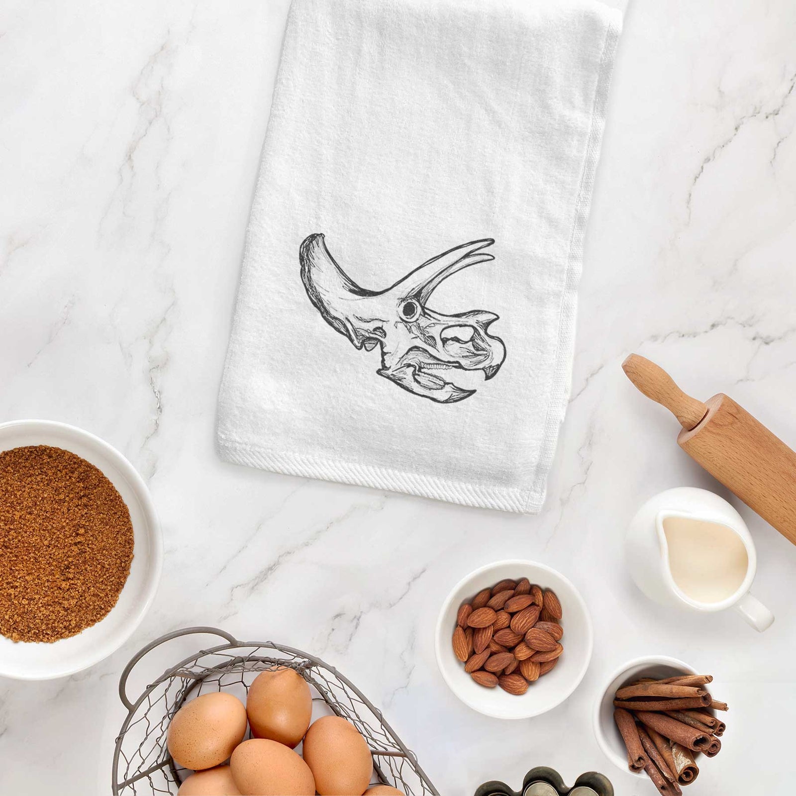 White hand towel printed with a detailed black ink illustration of a Triceratops skull with its horns and frill.
