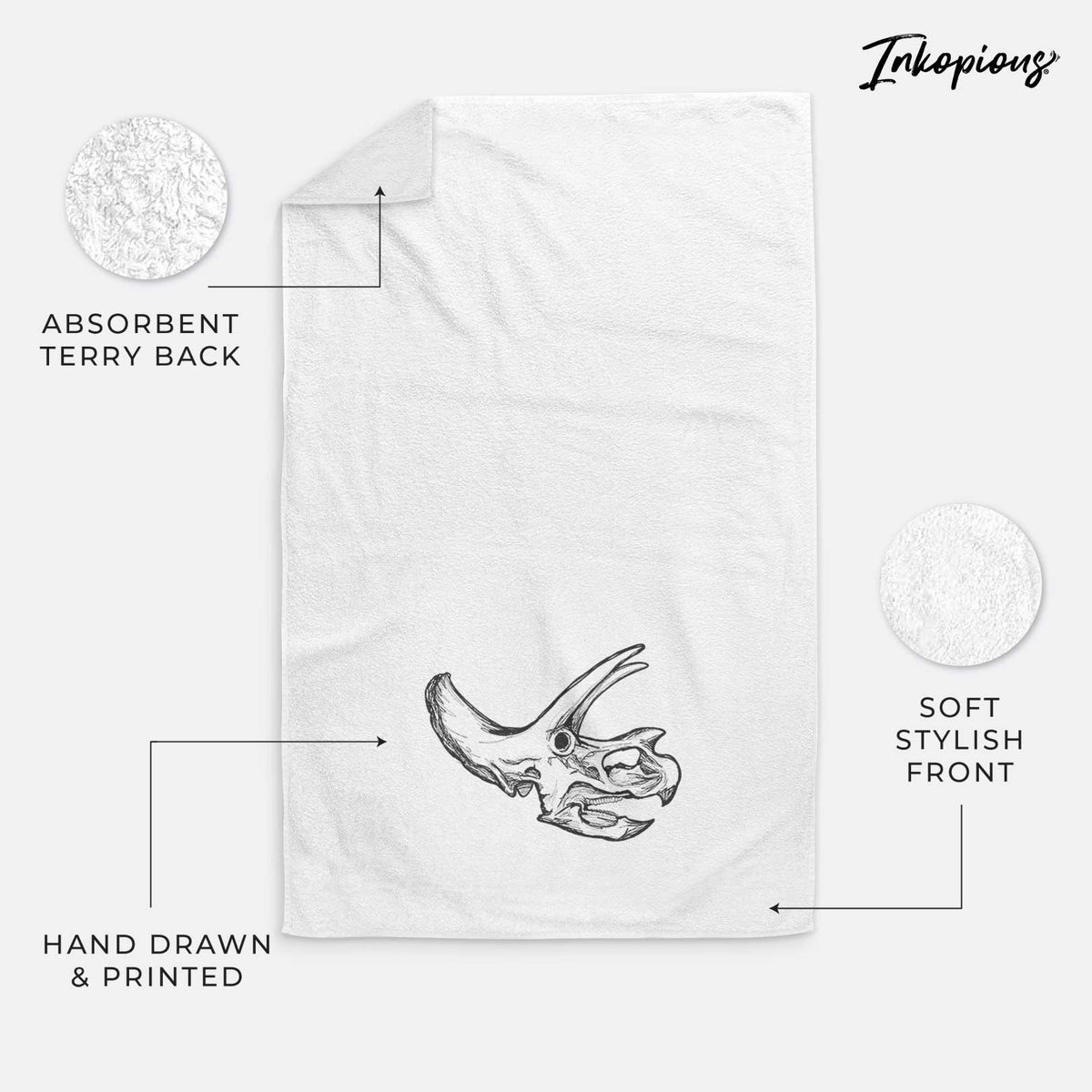 White hand towel printed with a detailed black ink illustration of a Triceratops skull with its horns and frill.
