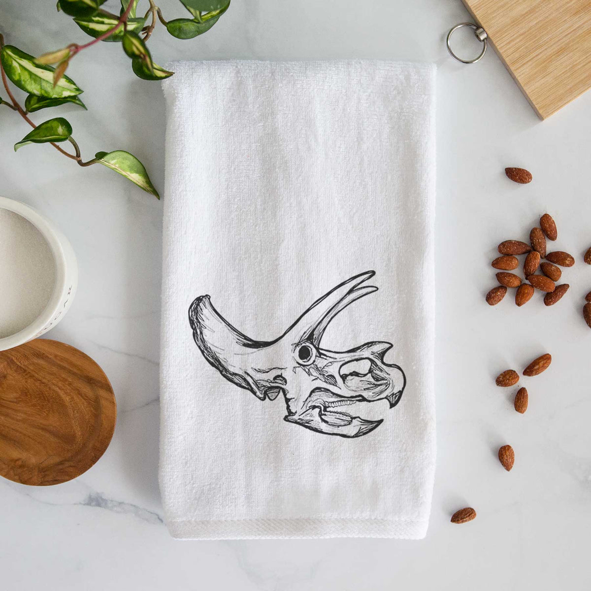 White hand towel printed with a detailed black ink illustration of a Triceratops skull with its horns and frill.