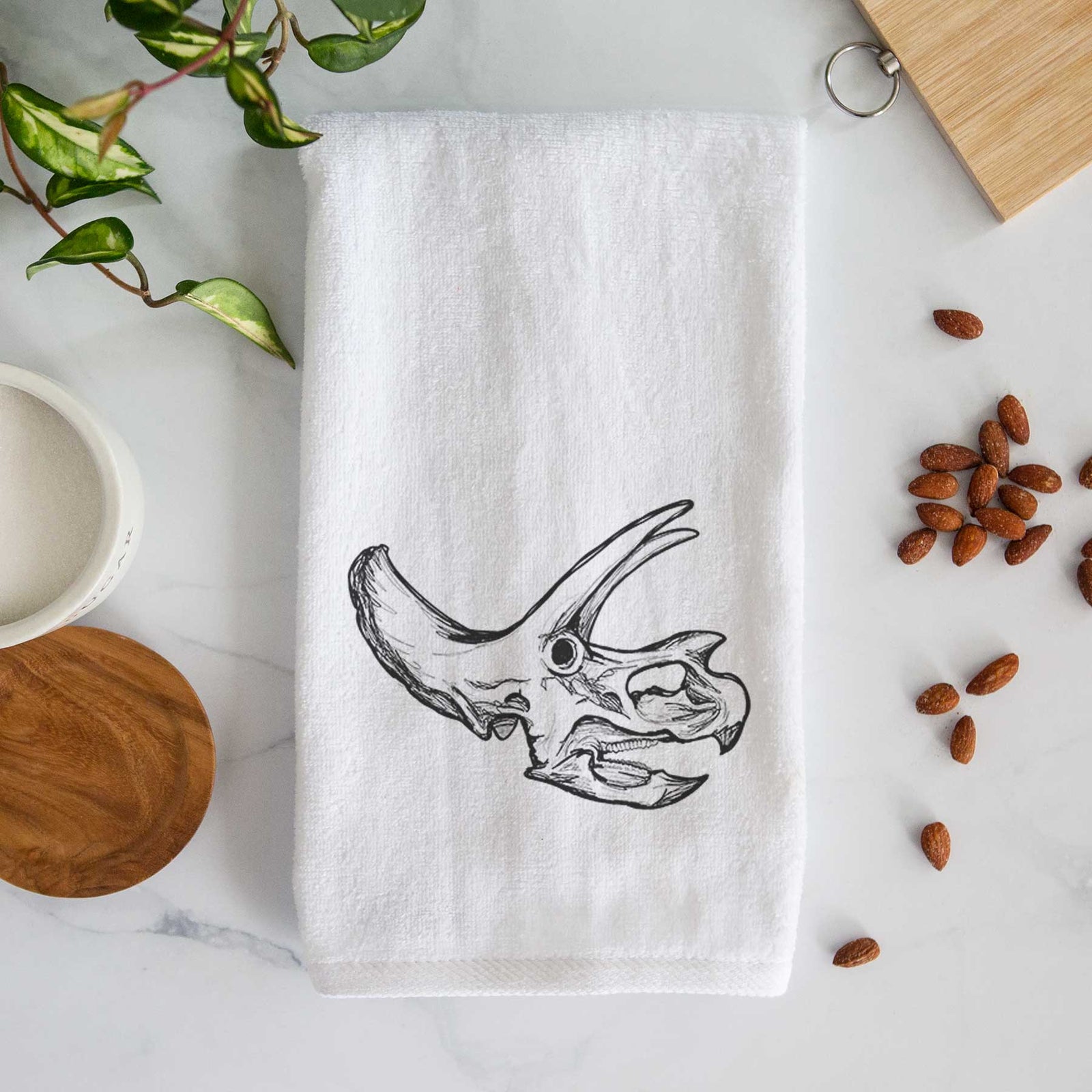 White hand towel printed with a detailed black ink illustration of a Triceratops skull with its horns and frill.