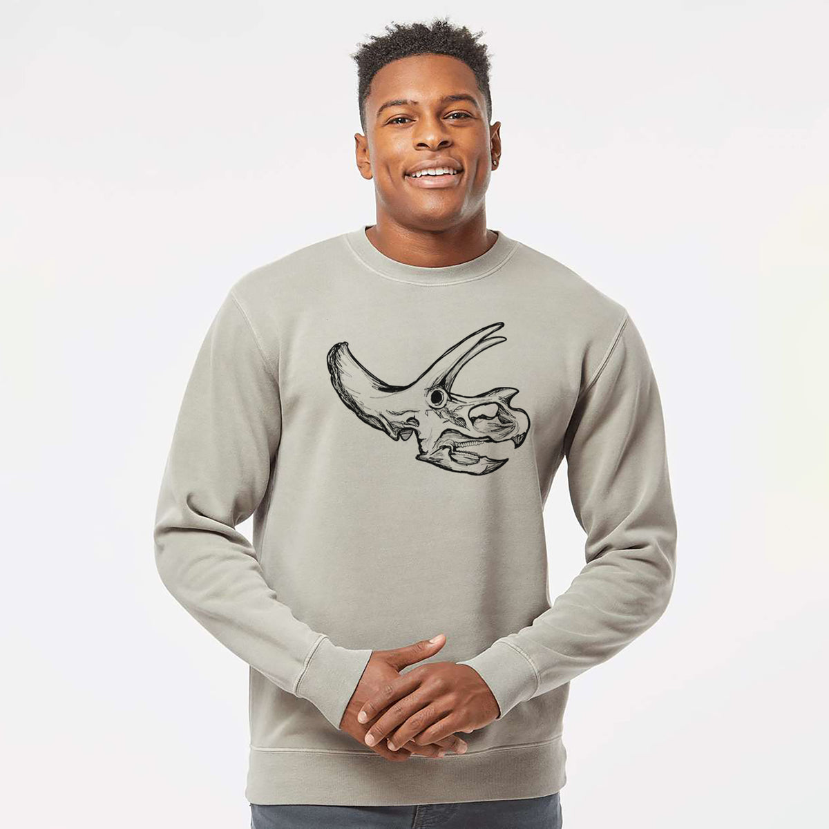 Model wearing a cement grey pigment dyed crewneck sweatshirt printed with a detailed black ink illustration of a Triceratops skull with its horns and frill.