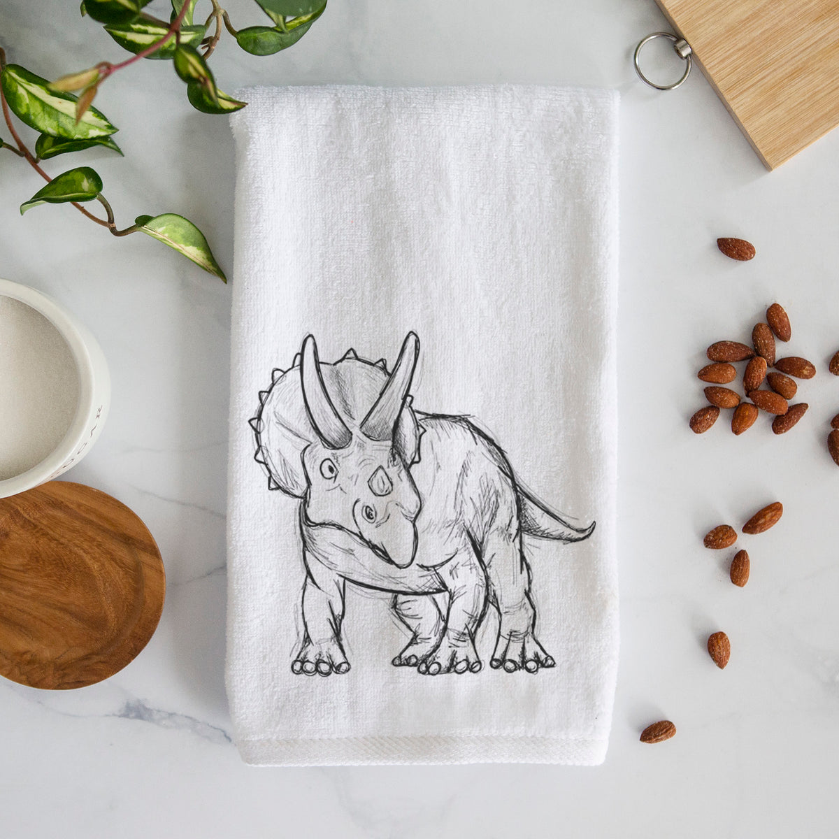 White hand towel printed with a black ink illustration of a Triceratops walking.