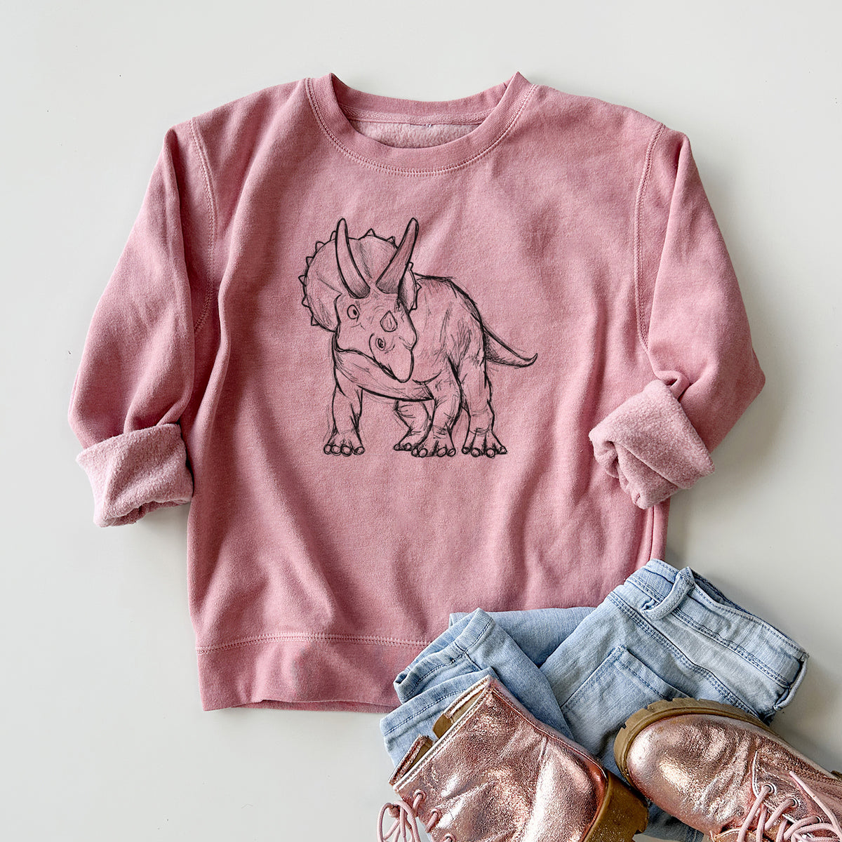 Youth crewneck sweatshirt printed with a black ink illustration of a Triceratops walking, styled flat with jeans and boots.