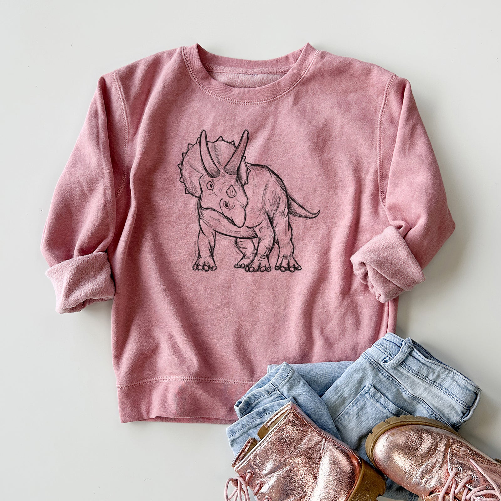 Boy wearing a youth crewneck sweatshirt printed with a black ink illustration of a Triceratops walking, outdoors.