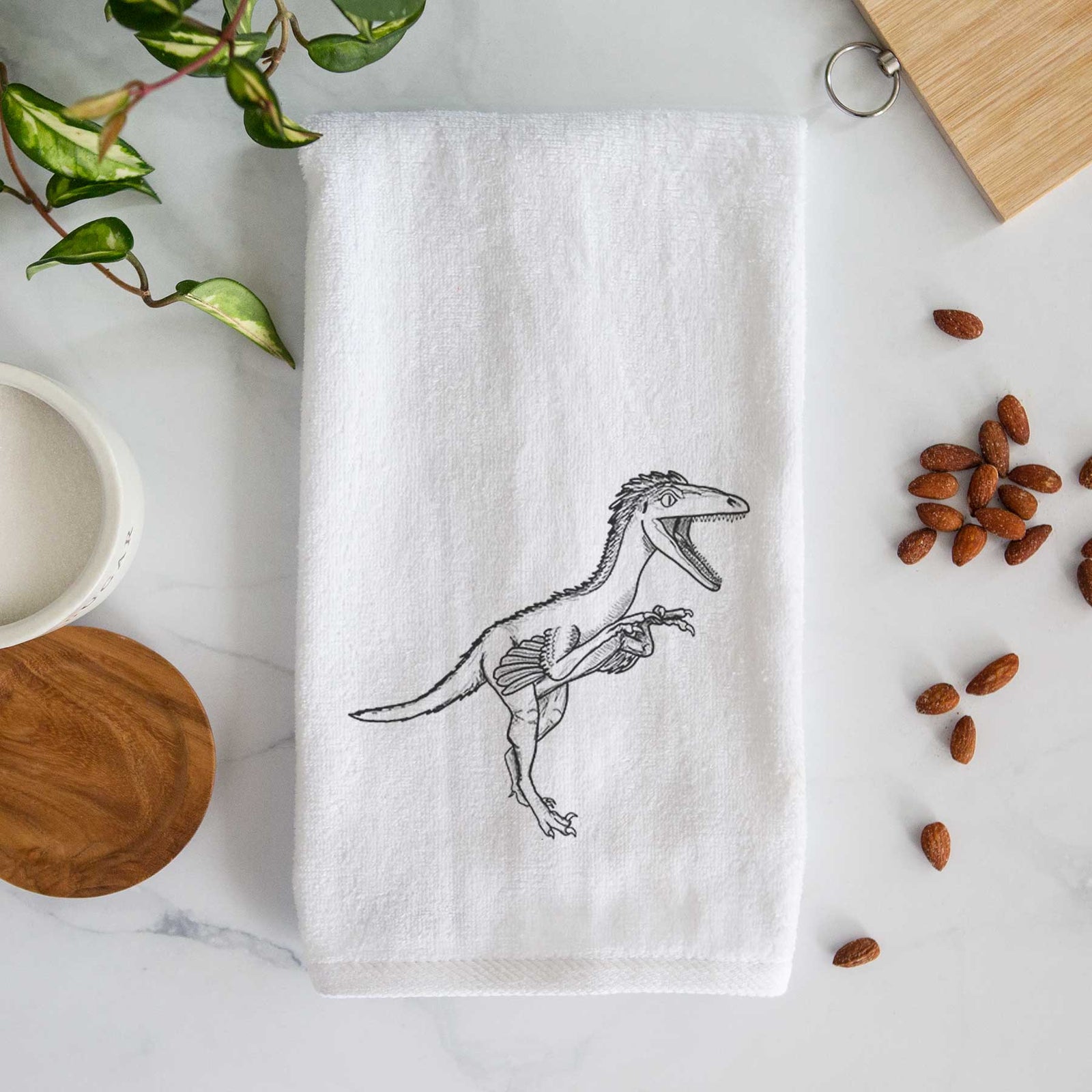 White hand towel printed with a black ink illustration of a Troodon dinosaur running.