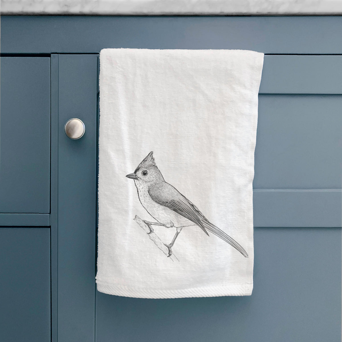 White hand towel printed with a detailed black ink sketch of a tufted titmouse perched on a branch, hanging on a cabinet door.