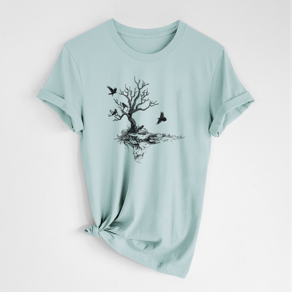 Dusty blue lightweight cotton t-shirt laid flat with the sleeves rolled, printed with a black ink illustration of a bare twisted tree on a small island with ravens flying around it.