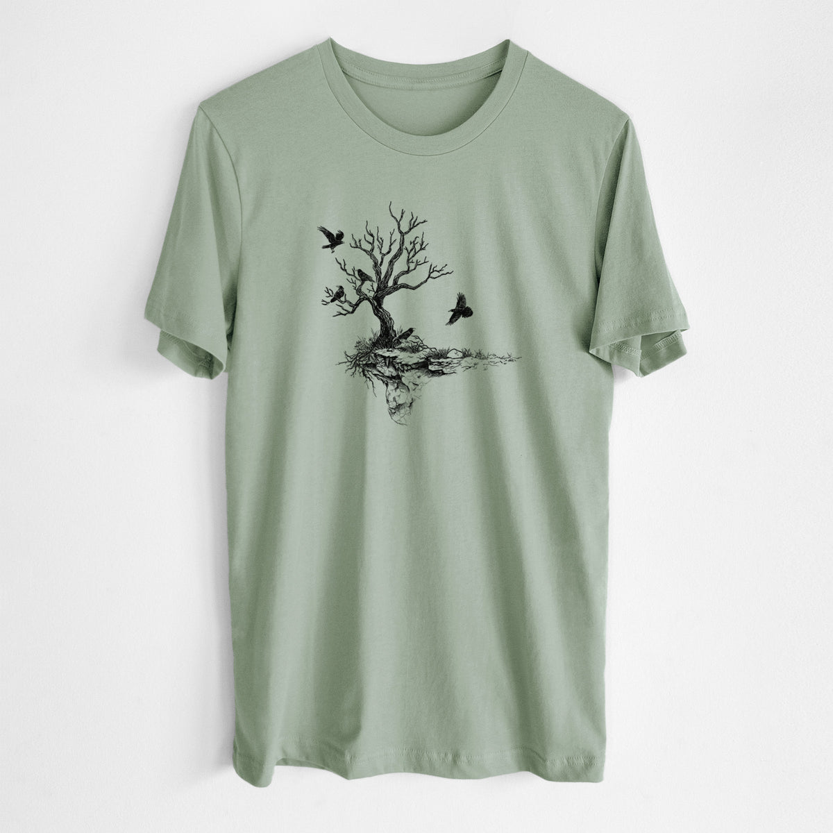 Sage green lightweight cotton t-shirt laid flat, printed with a black ink illustration of a bare twisted tree on a small island with ravens flying around it.