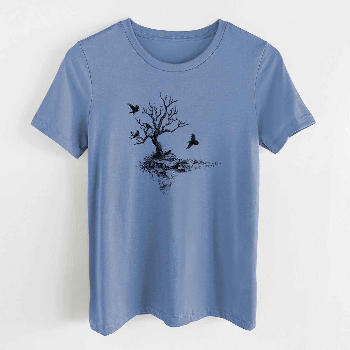 Blue bell women's relaxed fit cotton t-shirt laid flat, printed with a black ink illustration of a bare twisted tree on a small island with ravens flying around it.