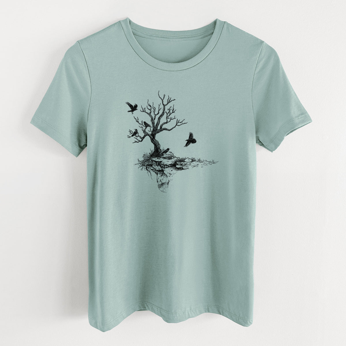 Dusty blue women's relaxed fit cotton t-shirt laid flat, printed with a black ink illustration of a bare twisted tree on a small island with ravens flying around it.