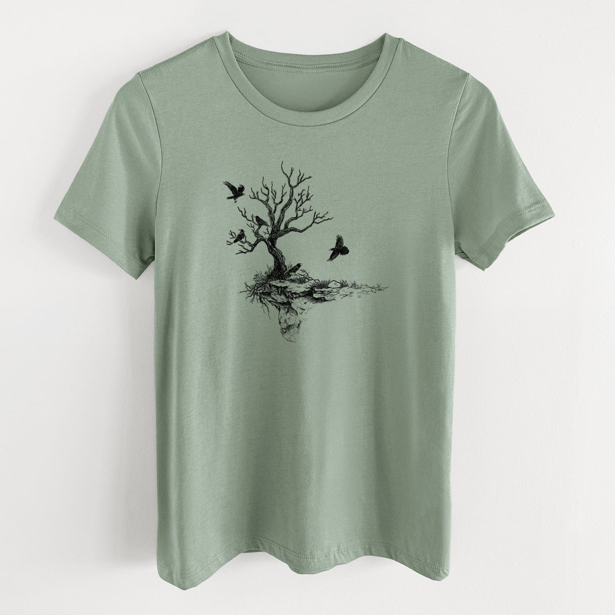 Sage green women's relaxed fit cotton t-shirt laid flat, printed with a black ink illustration of a bare twisted tree on a small island with ravens flying around it.