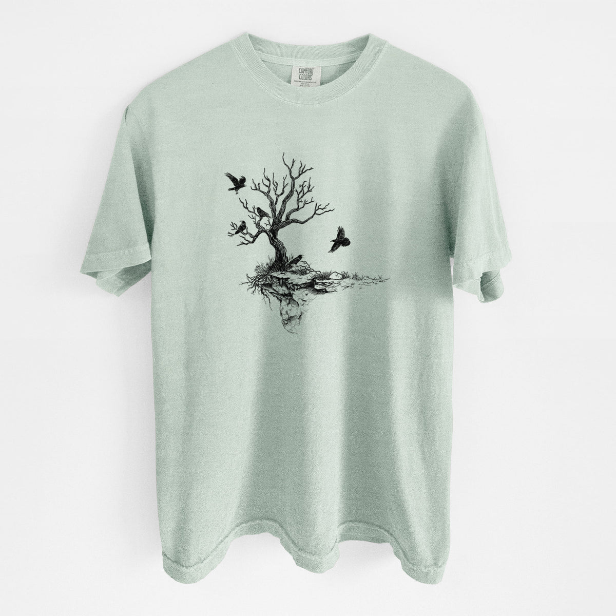 Bay green Comfort Colors t-shirt laid flat, printed with a black ink illustration of a bare twisted tree on a small island with ravens flying around it.