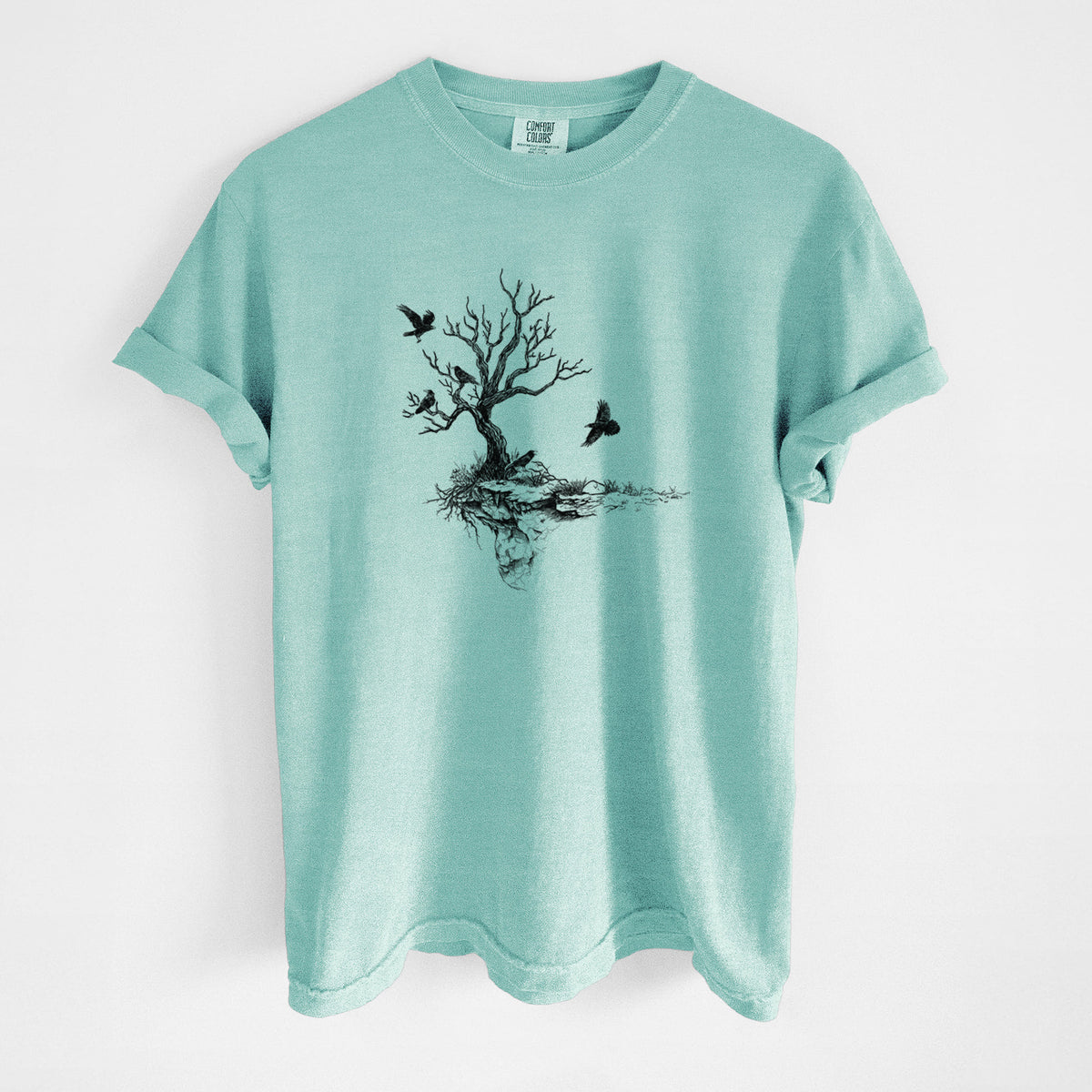 Chalky mint Comfort Colors t-shirt laid flat, printed with a black ink illustration of a bare twisted tree on a small island with ravens flying around it.