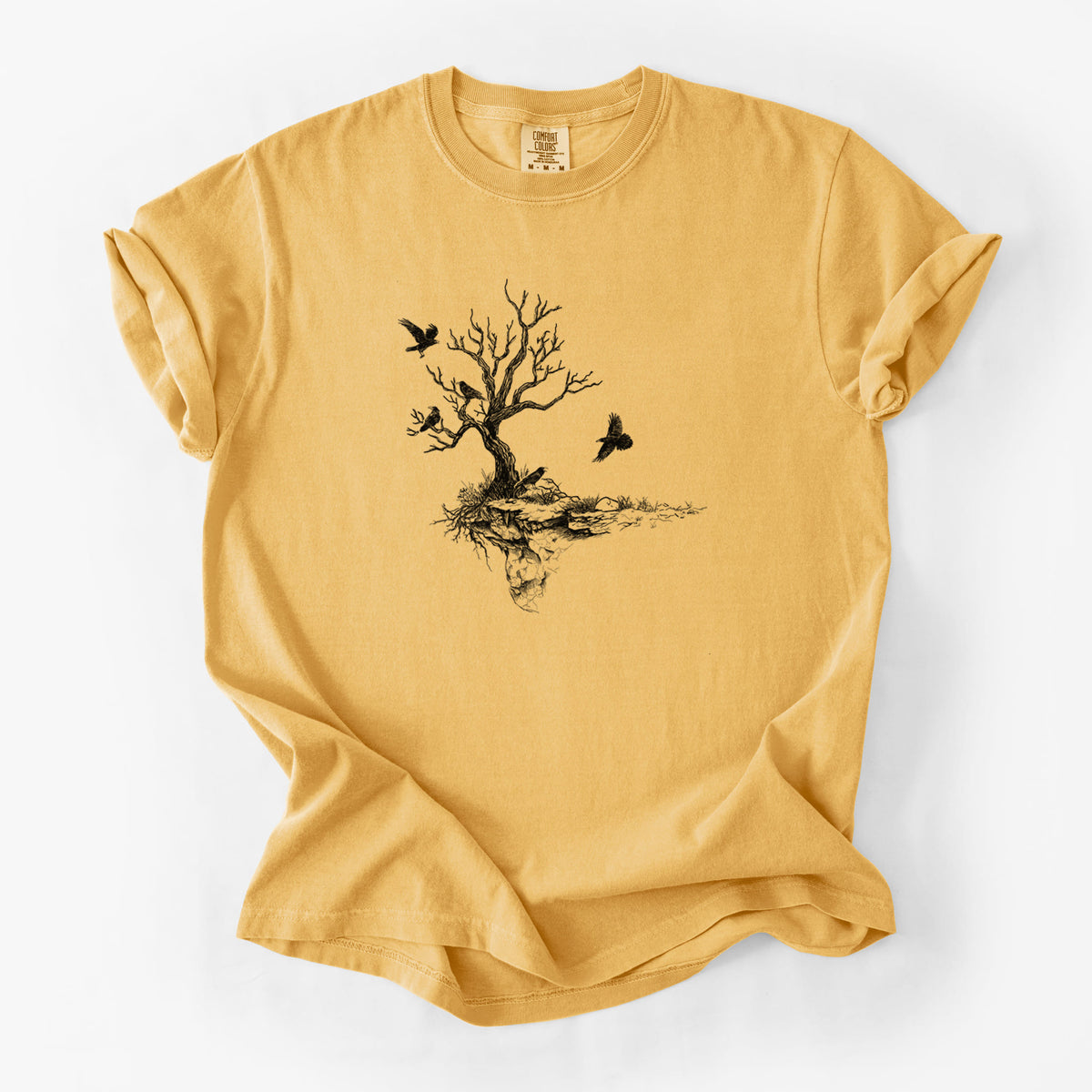 Golden wheat yellow Comfort Colors t-shirt laid flat, printed with a black ink illustration of a bare twisted tree on a small island with ravens flying around it.