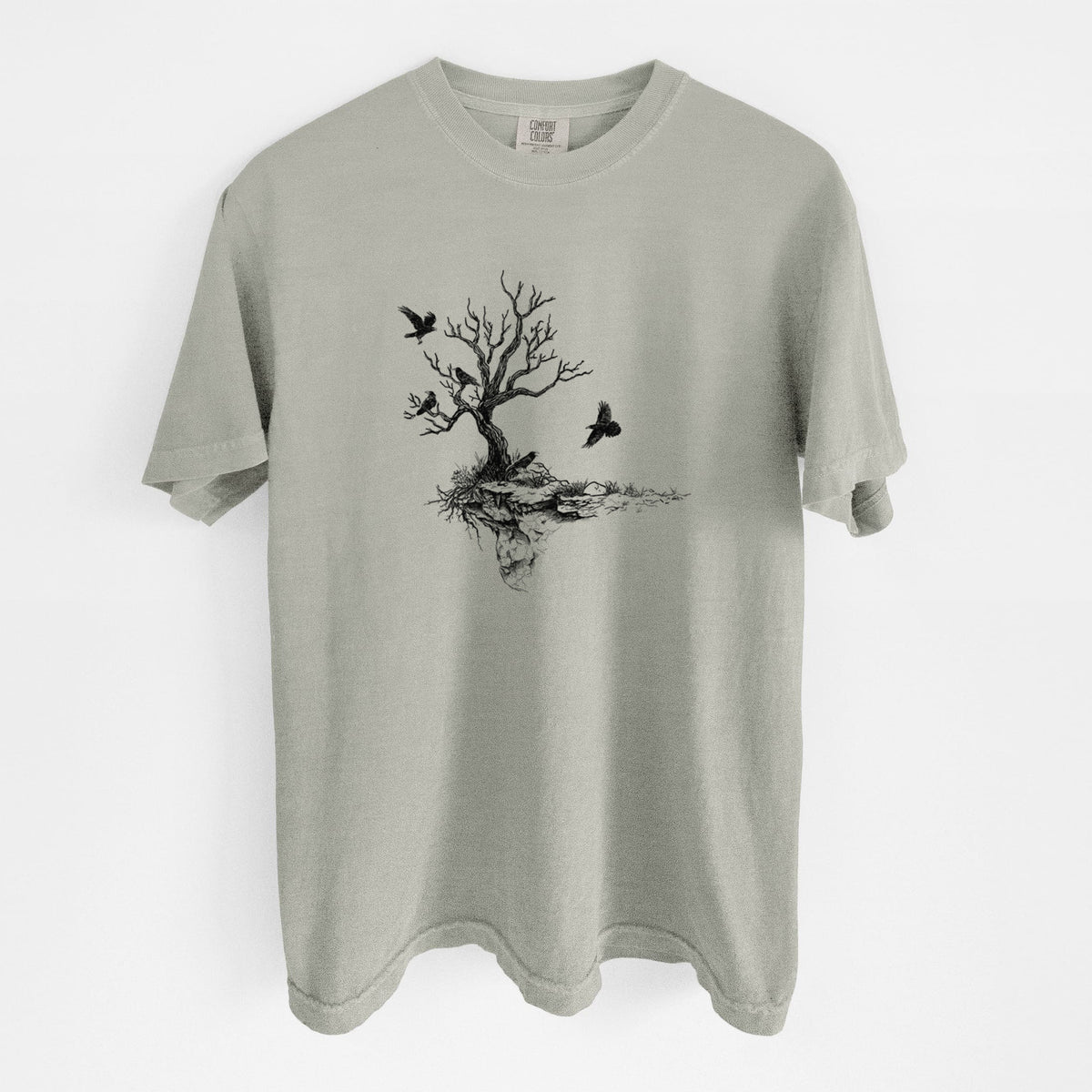 Sandstone beige Comfort Colors t-shirt laid flat, printed with a black ink illustration of a bare twisted tree on a small island with ravens flying around it.