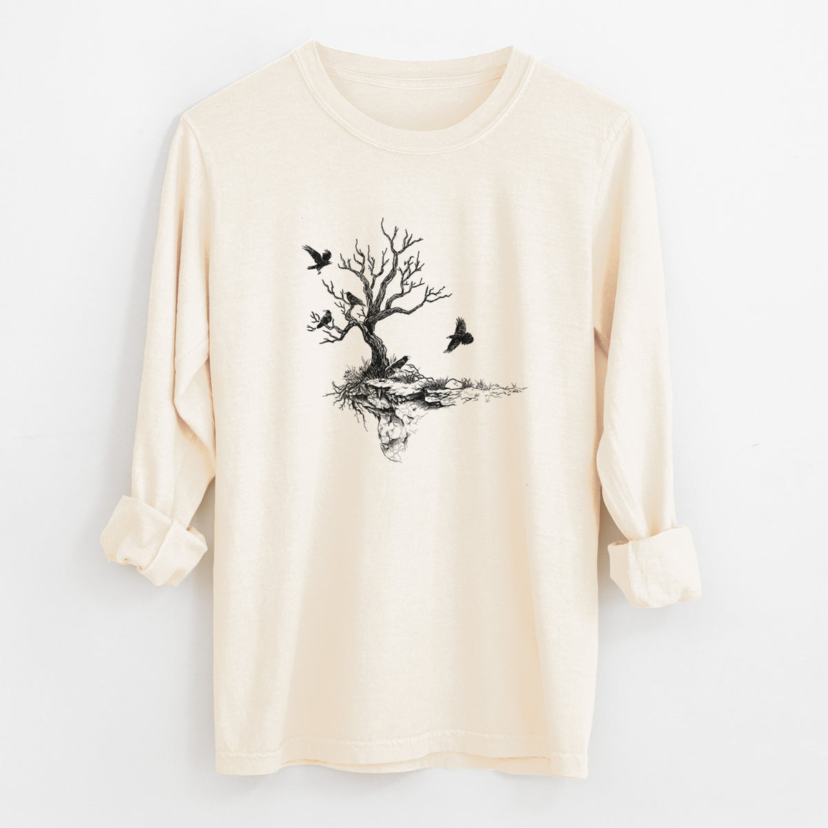 Ivory Comfort Colors long sleeve shirt laid flat with the cuffs rolled, printed with a black ink illustration of a bare twisted tree on a small island with ravens flying around it.