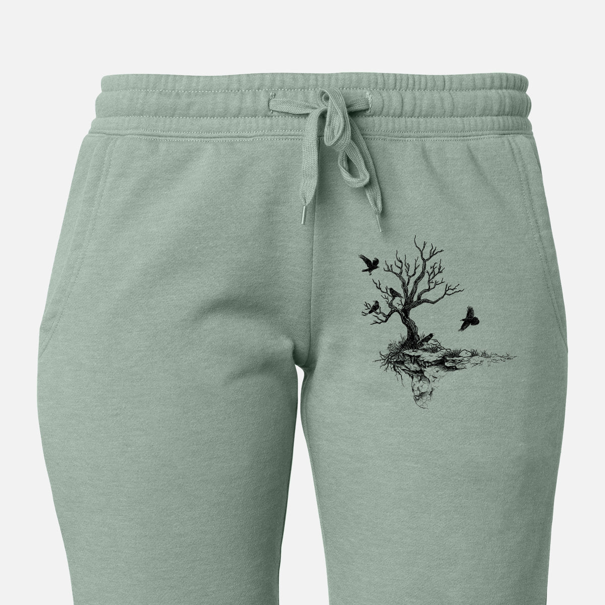 Front of sage green Cali Wave sweatpants, printed with a black ink illustration of a bare twisted tree on a small island with ravens flying around it on the leg.