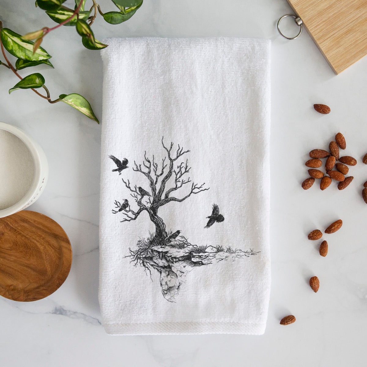 White hand towel printed with a black ink illustration of a bare twisted tree on a small island with ravens flying around it.