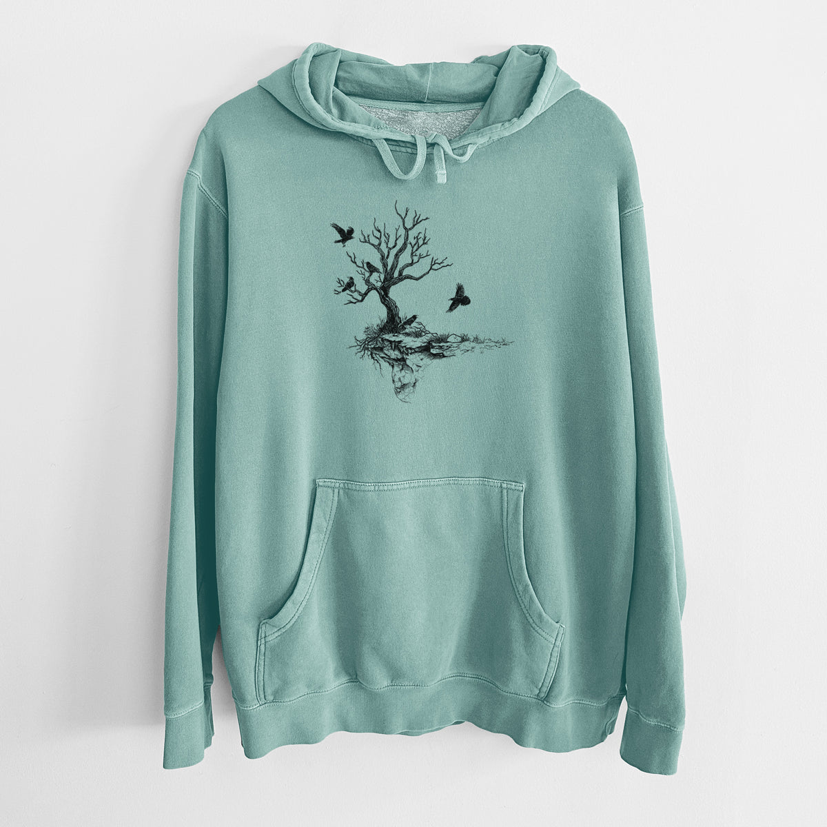 Mint green pigment dyed hoodie laid flat, printed with a black ink illustration of a bare twisted tree on a small island with ravens flying around it.