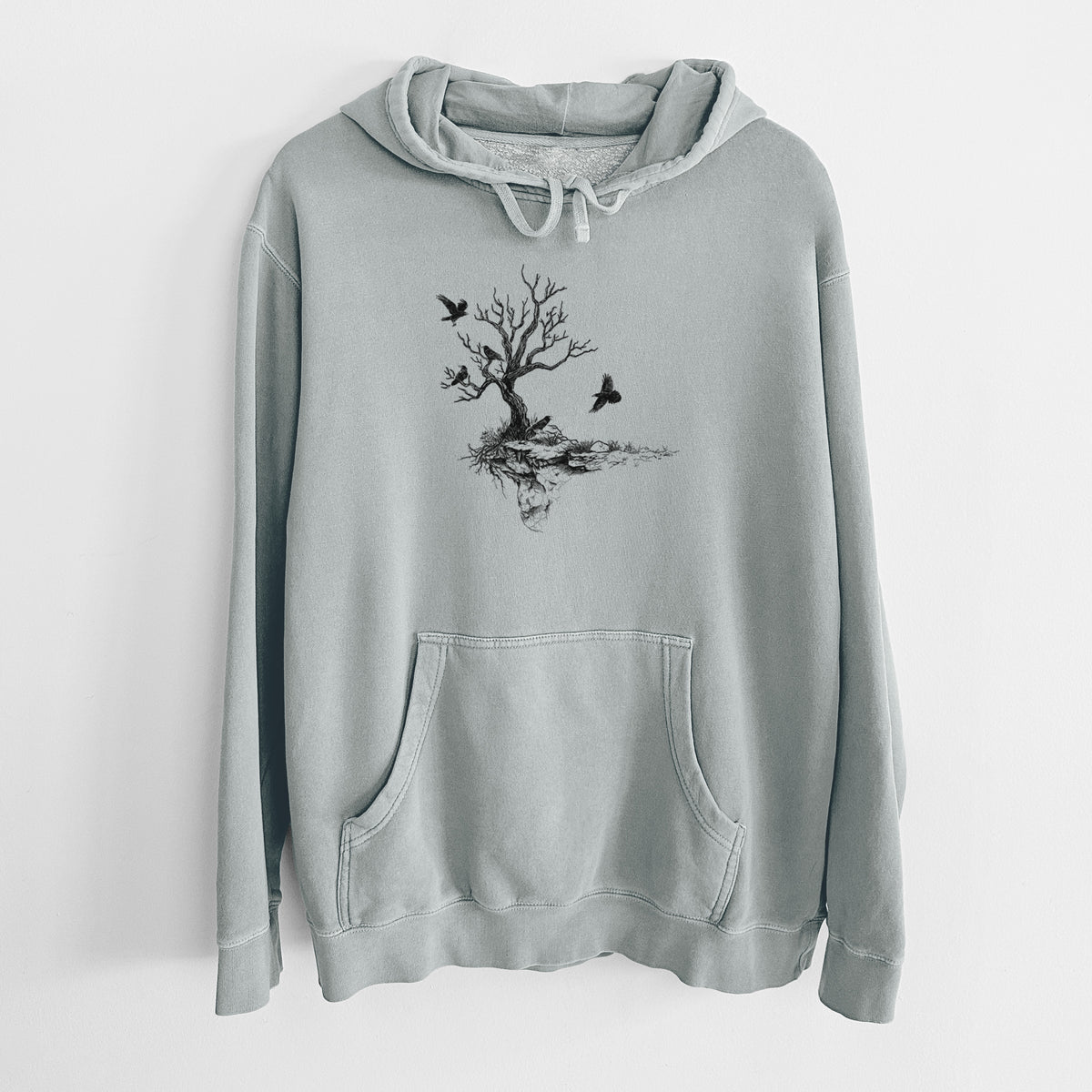 Sage green pigment dyed hoodie laid flat, printed with a black ink illustration of a bare twisted tree on a small island with ravens flying around it.