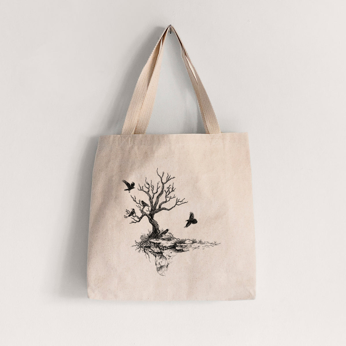 Natural canvas tote bag printed with a black ink illustration of a bare twisted tree on a small island with ravens flying around it.