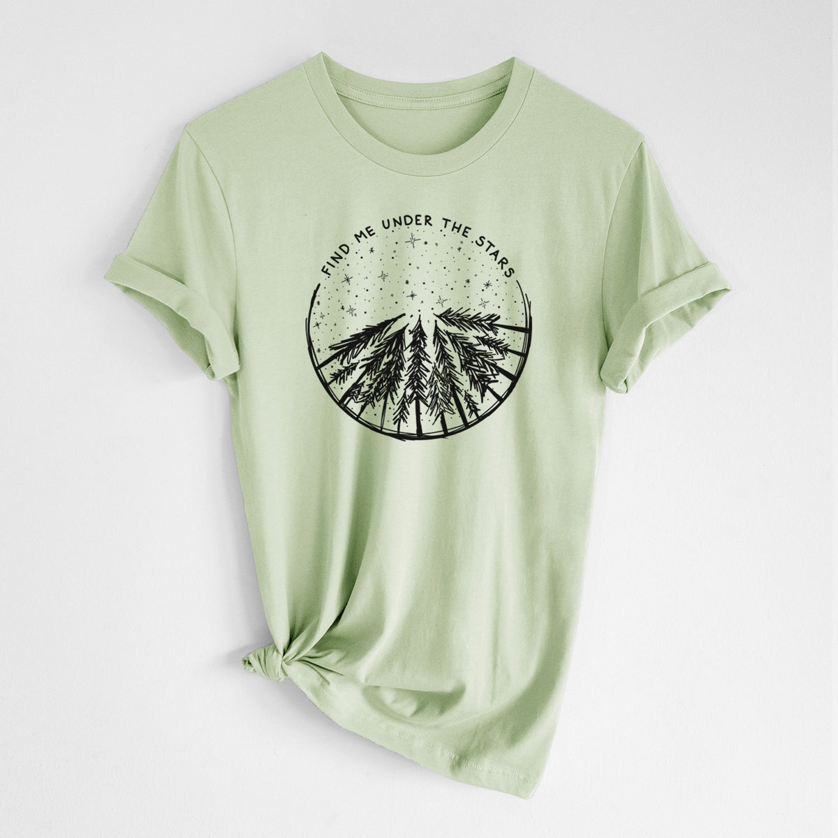 Spring green lightweight cotton t-shirt laid flat with the sleeves rolled, printed with a circle of pine trees under a starry sky, with the words Find Me Under the Stars.