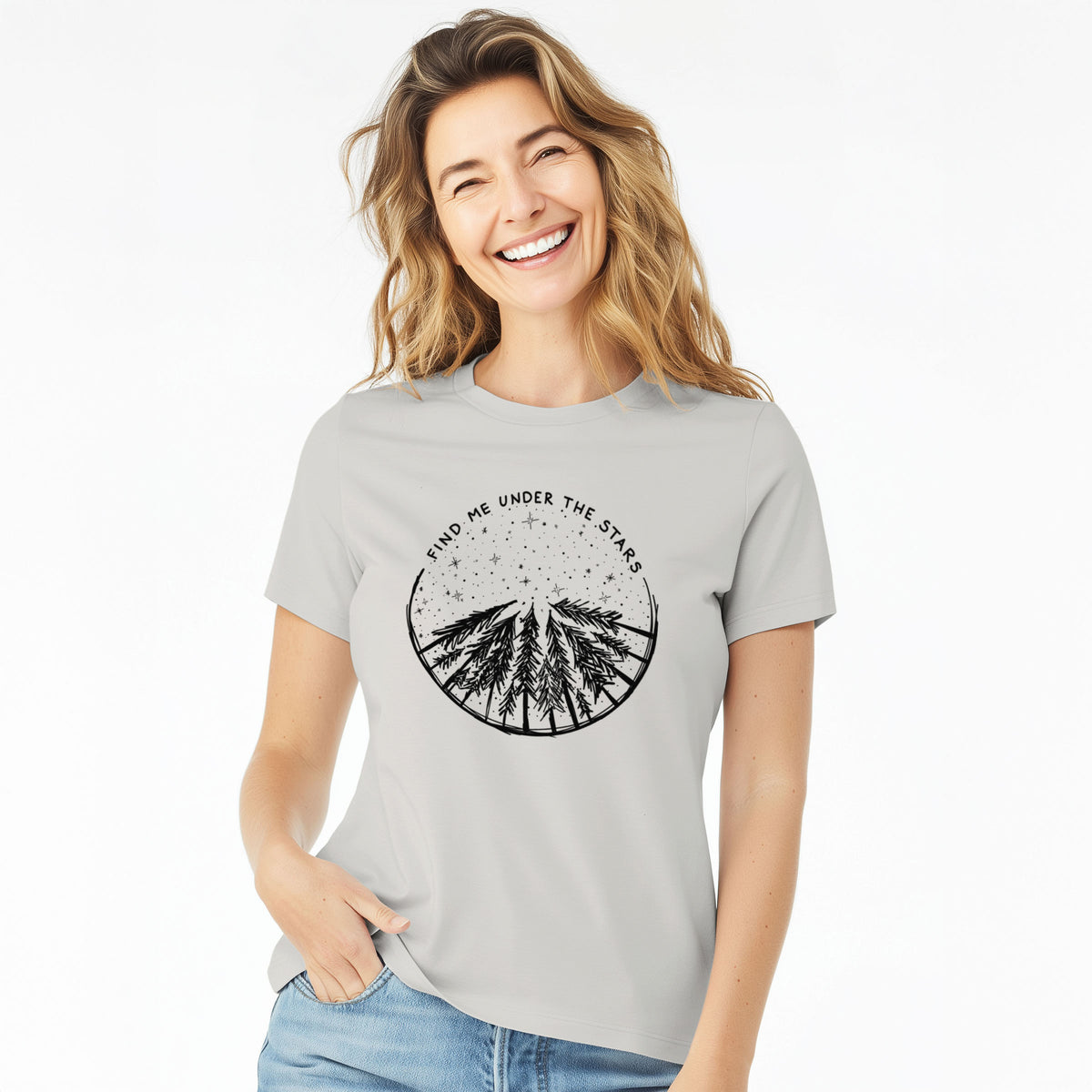 Woman wearing a lunar grey women's relaxed fit cotton t-shirt printed with a circle of pine trees under a starry sky, with the words Find Me Under the Stars.