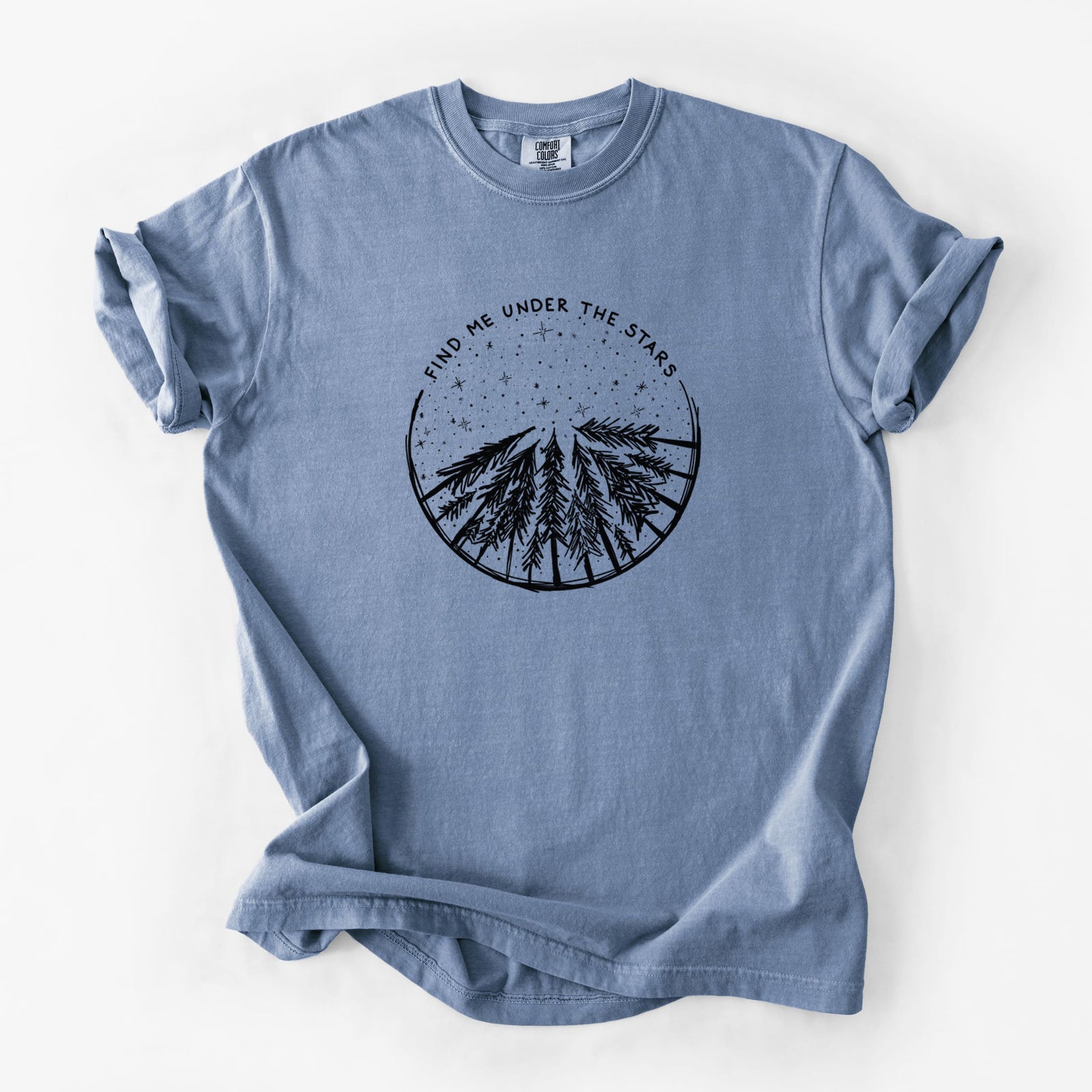 Blue jean Comfort Colors t-shirt laid flat, printed with a circle of pine trees under a starry sky, with the words Find Me Under the Stars.